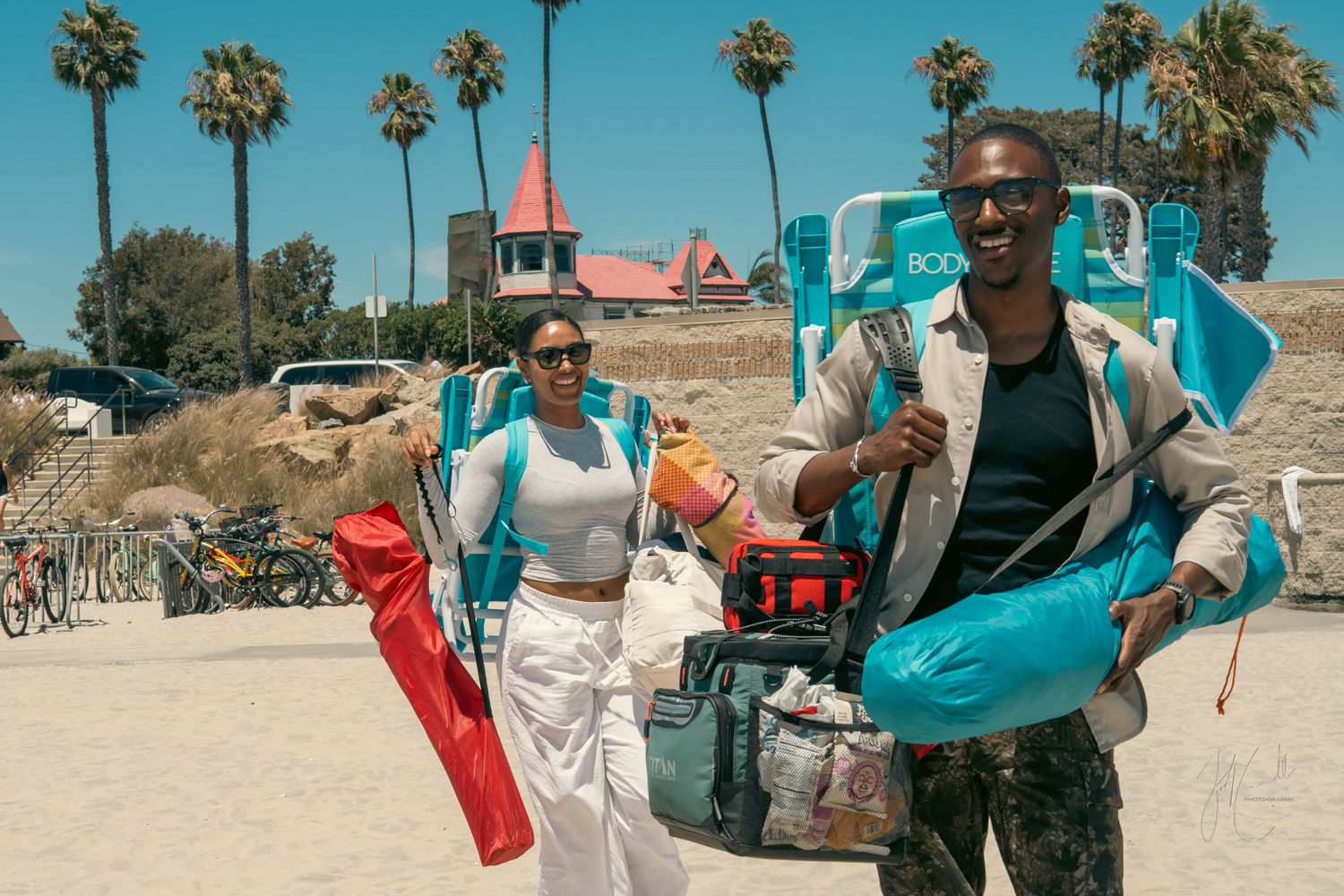 Palm trees line a sunny beach boardwalk with colorful beach accessories and activities.