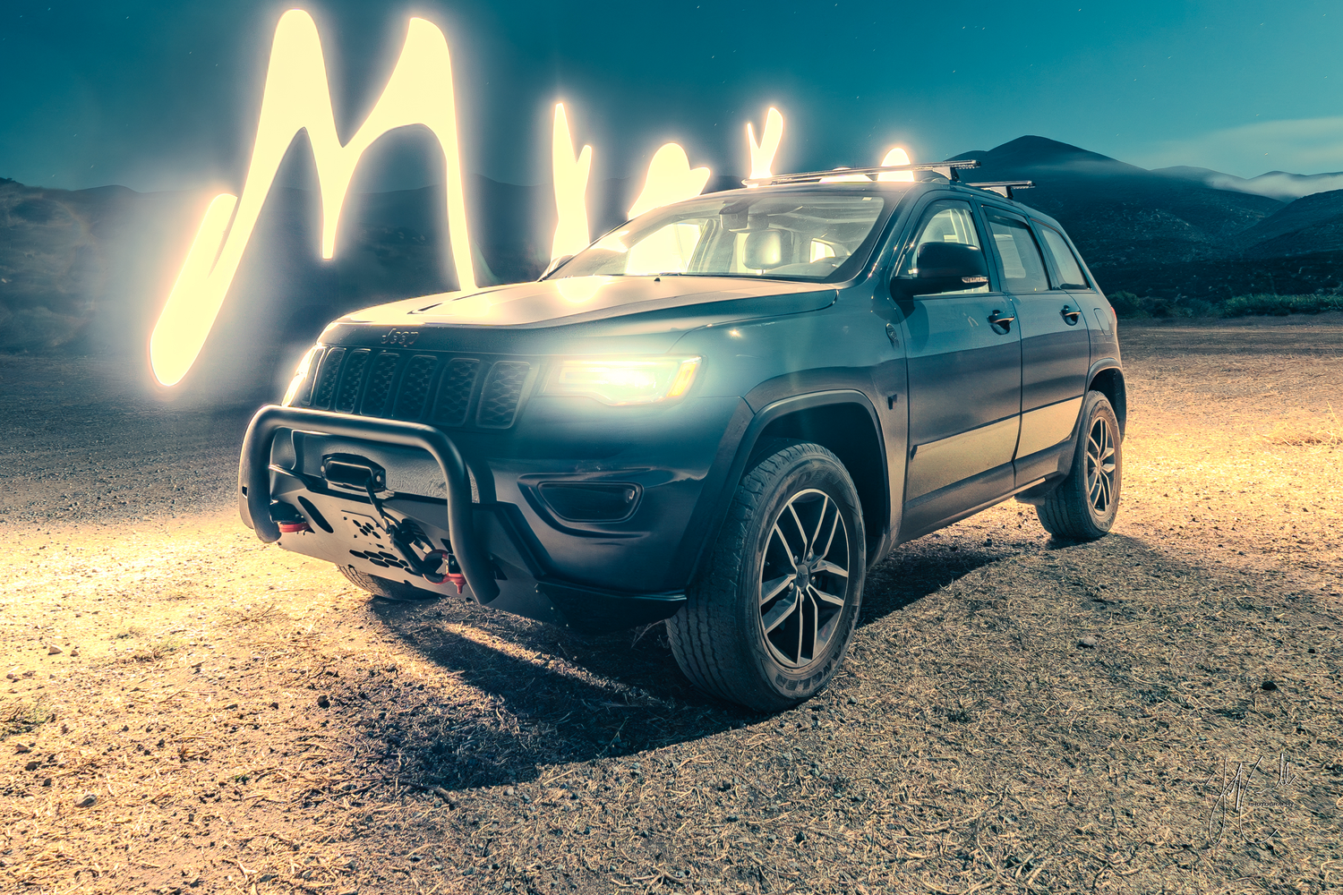 Car headlights illuminate a rocky desert terrain at night with dramatic shadows and lighting.
