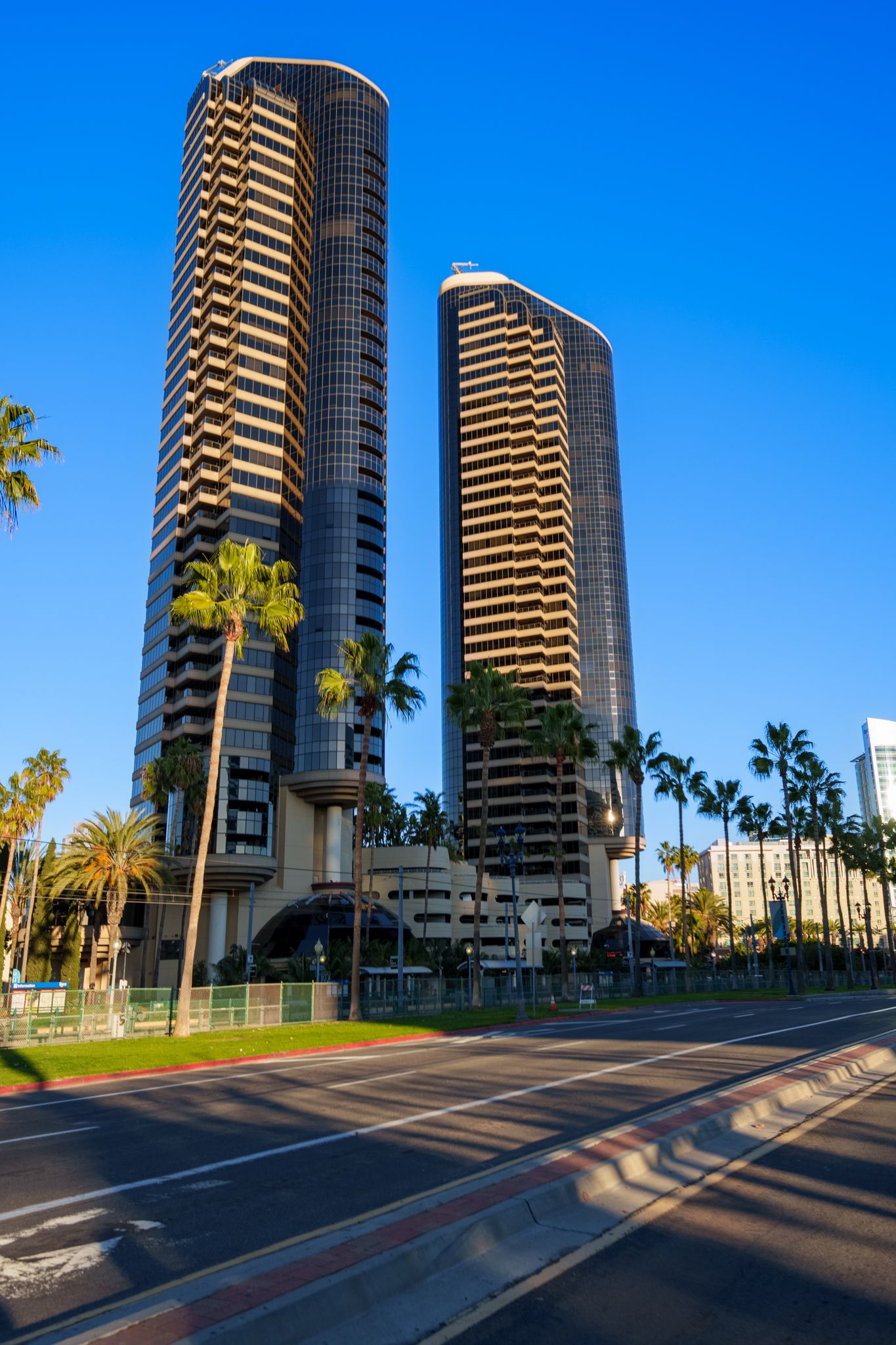 Two modern high-rise residential towers with palm trees along a street in San Diego against bright blue sky.