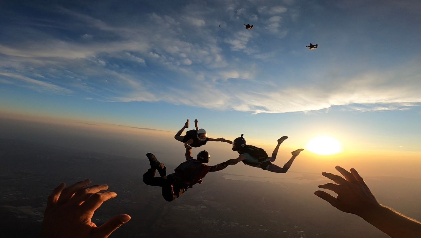 Silhouettes of skydivers performing maneuvers against a dramatic sunset sky.