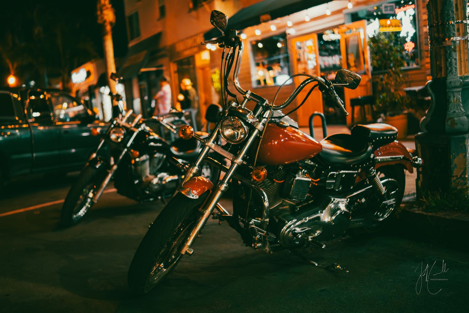 Row of parked motorcycles on city street at night with warm lighting.
