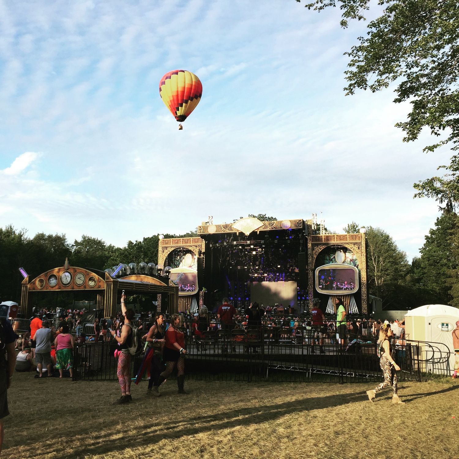 Hot air balloon floating over a festival ground with carnival rides and vendor booths at sunset.