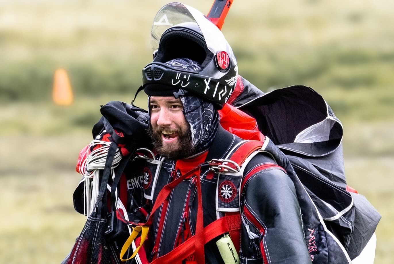 Skydiver in red suit and helmet preparing equipment during descent.