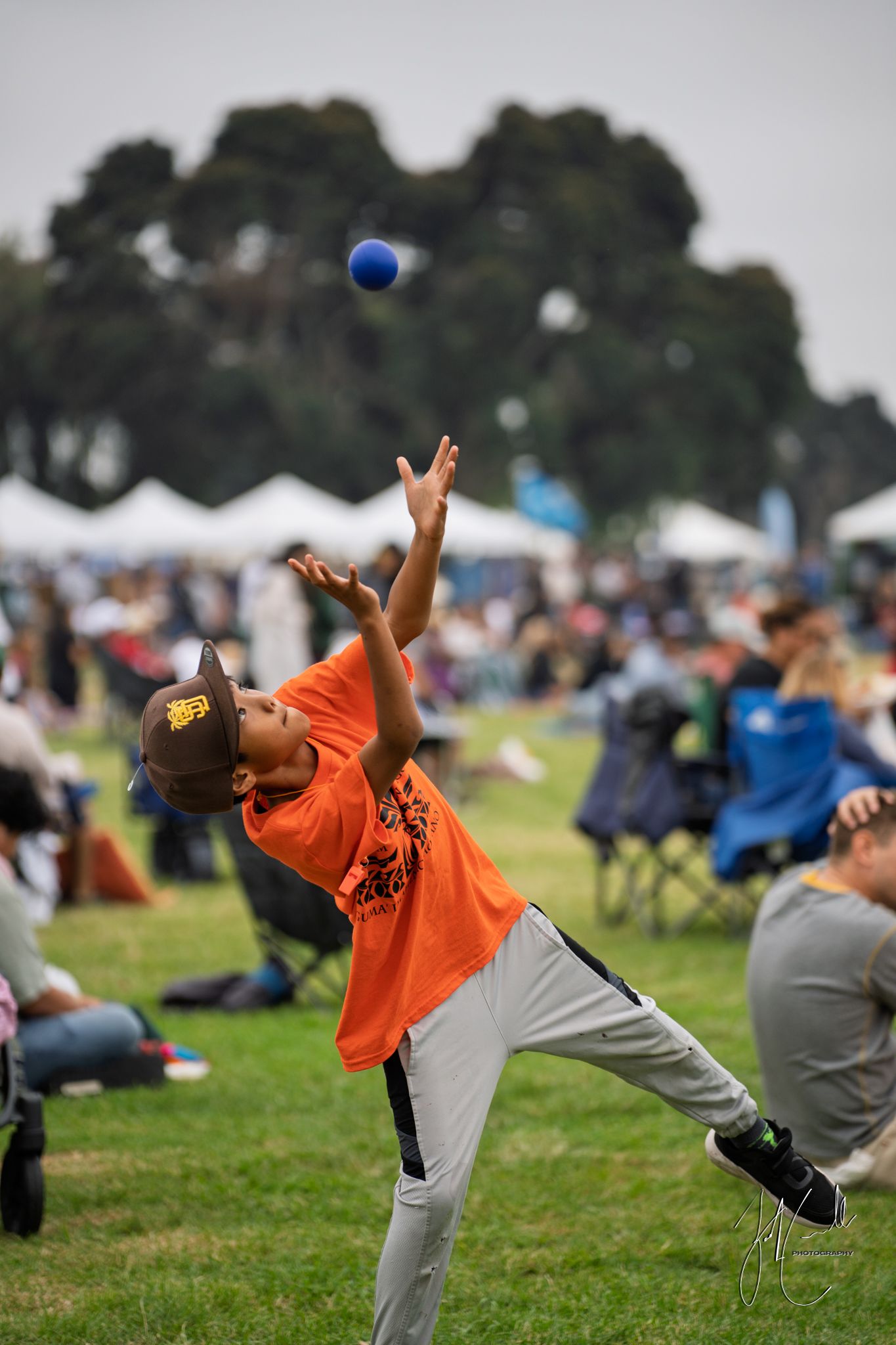 Person in orange shirt performing acrobatic moves catching a blue ball in a park.