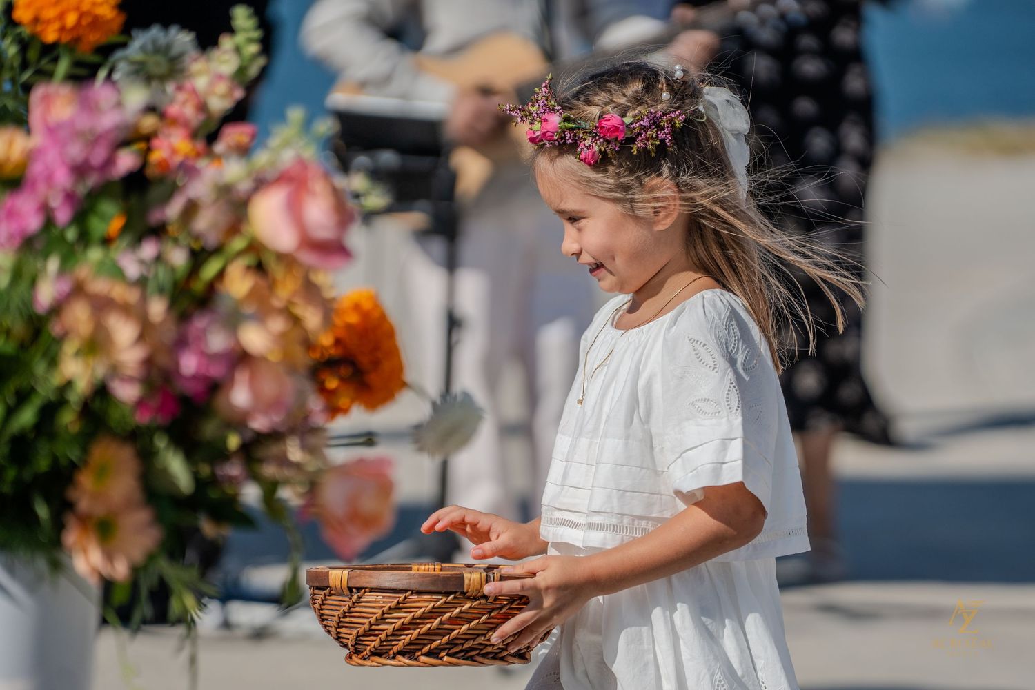 Young flower girls in white dresses hold baskets during an outdoor ceremony.