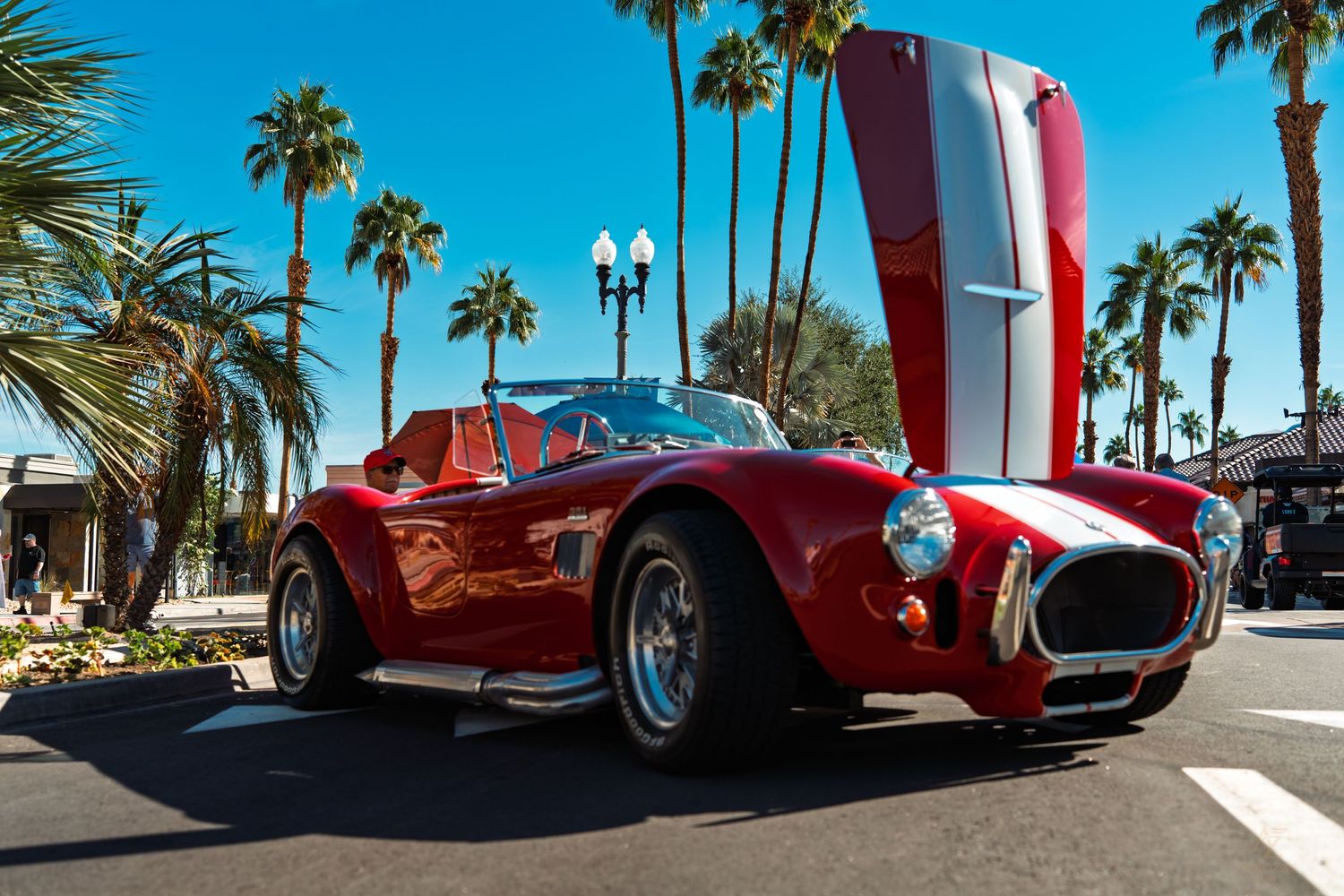 Classic red vintage sports car parked on a palm tree-lined street in a tropical location.