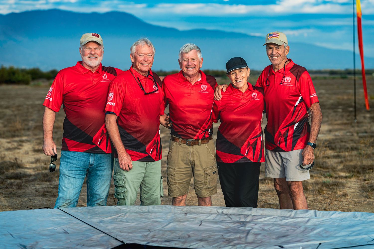 Group wearing red shirts posing together outdoors against a blue sky background.