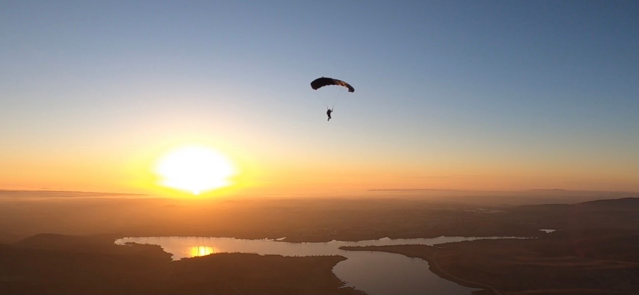 Panoramic view of a sunset over mountains with a paraglider in the distance.