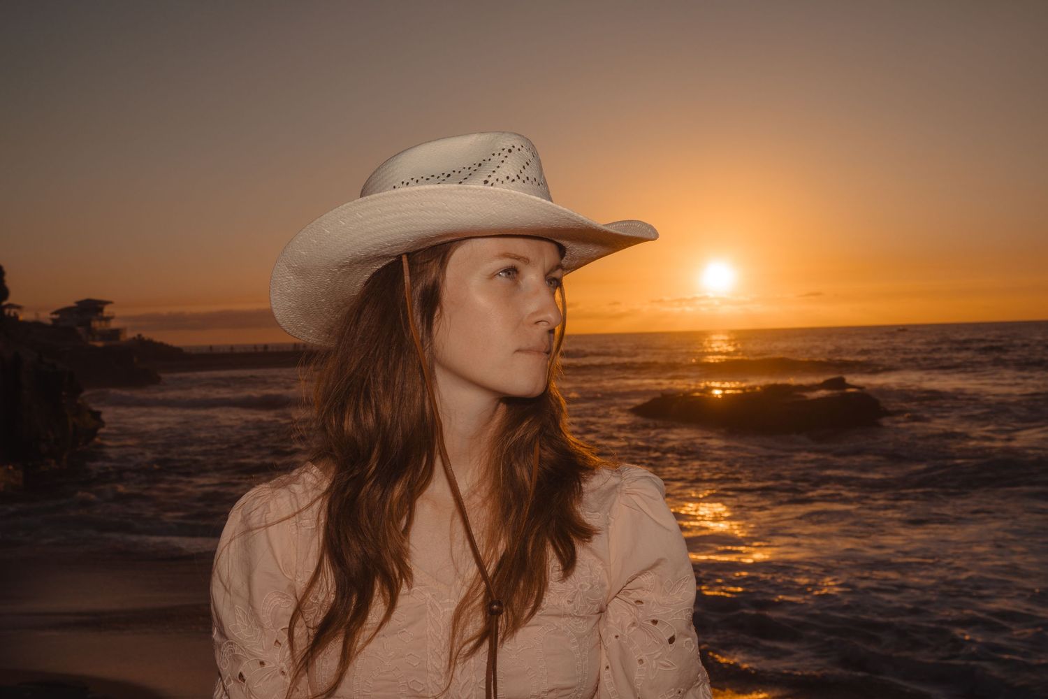 Silhouette of woman in cowboy hat against dramatic ocean sunset.