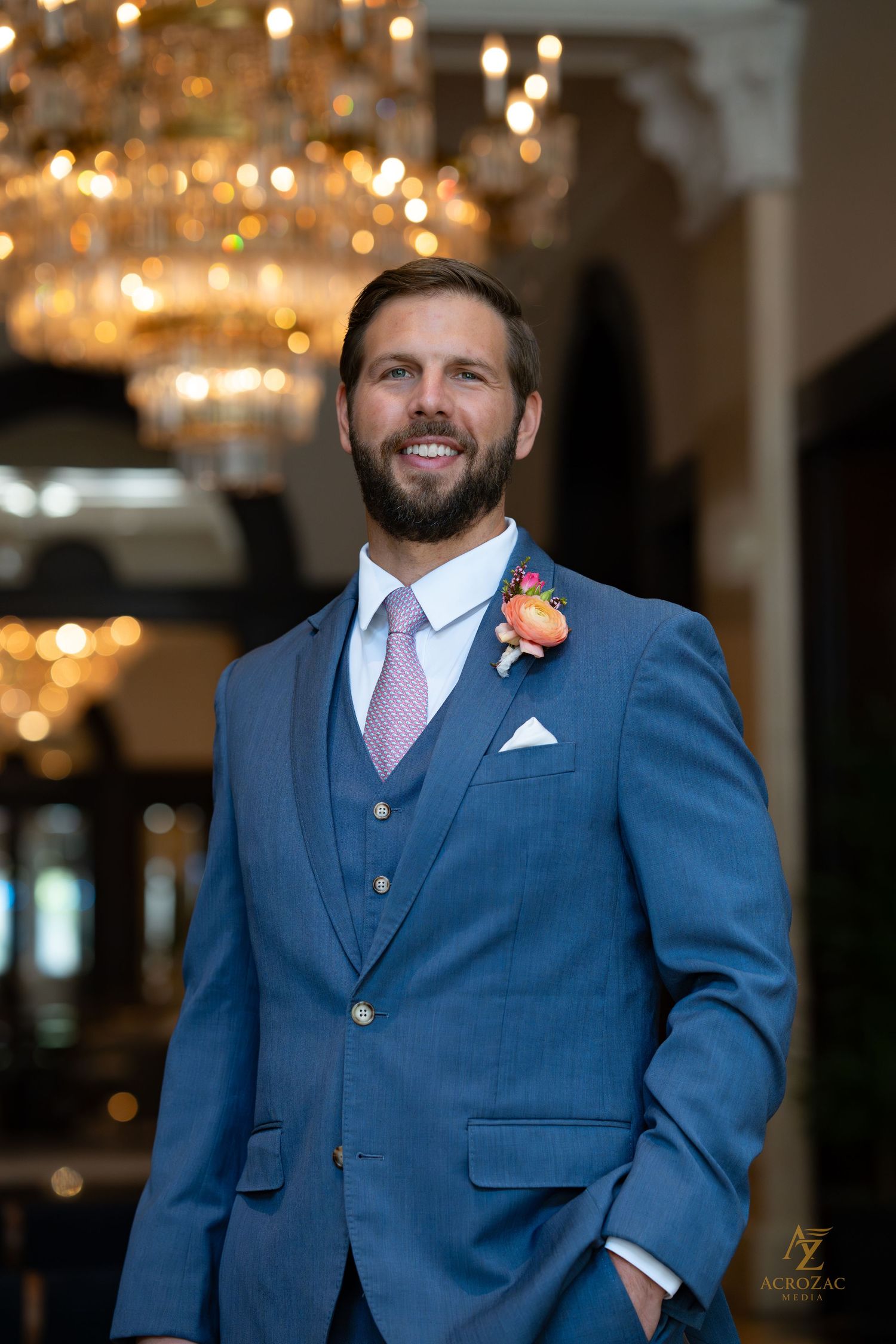 Wedding attire detail showing a navy blue suit with pink tie and coral boutonniere.