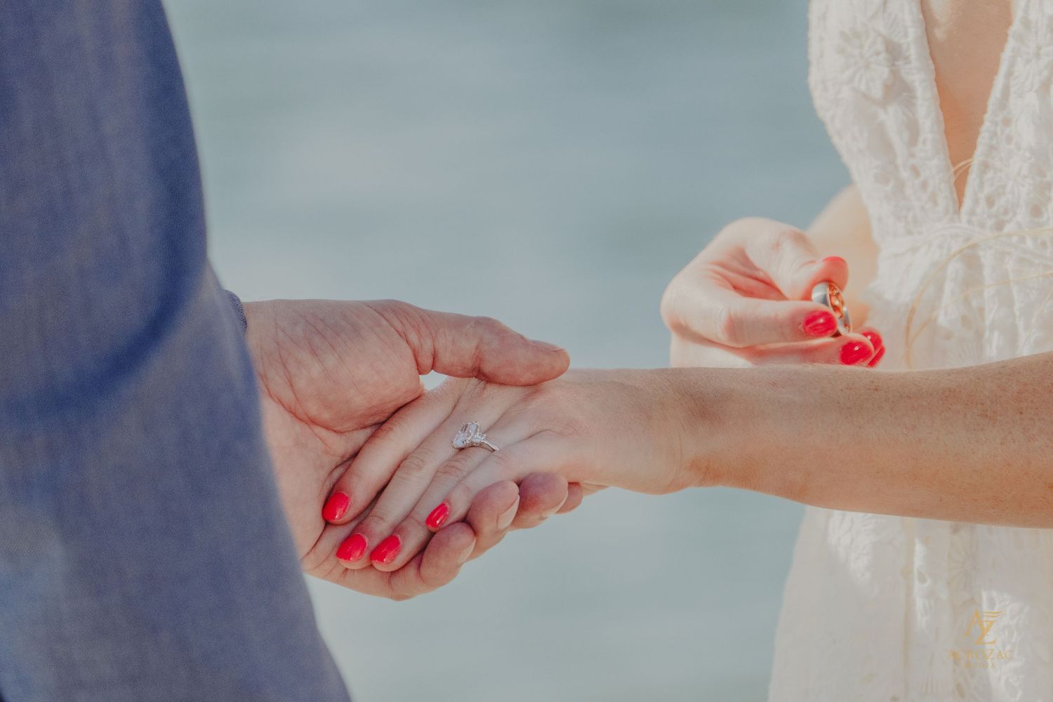 Close-up of hands exchanging rings during a wedding ceremony by the water.