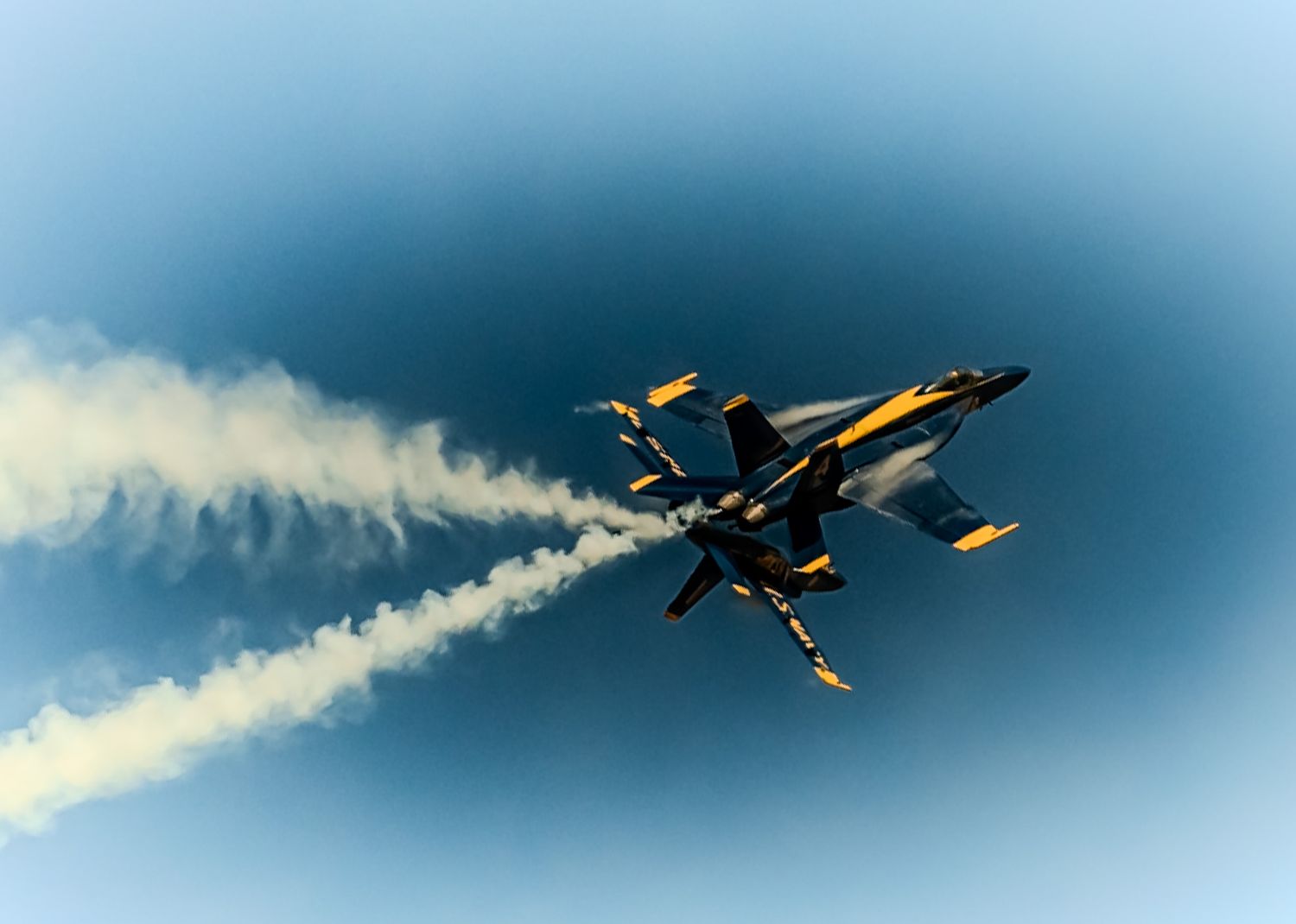 Navy Blue Angels F/A-18 Hornet fighter jet performing aerial maneuver with smoke trails.