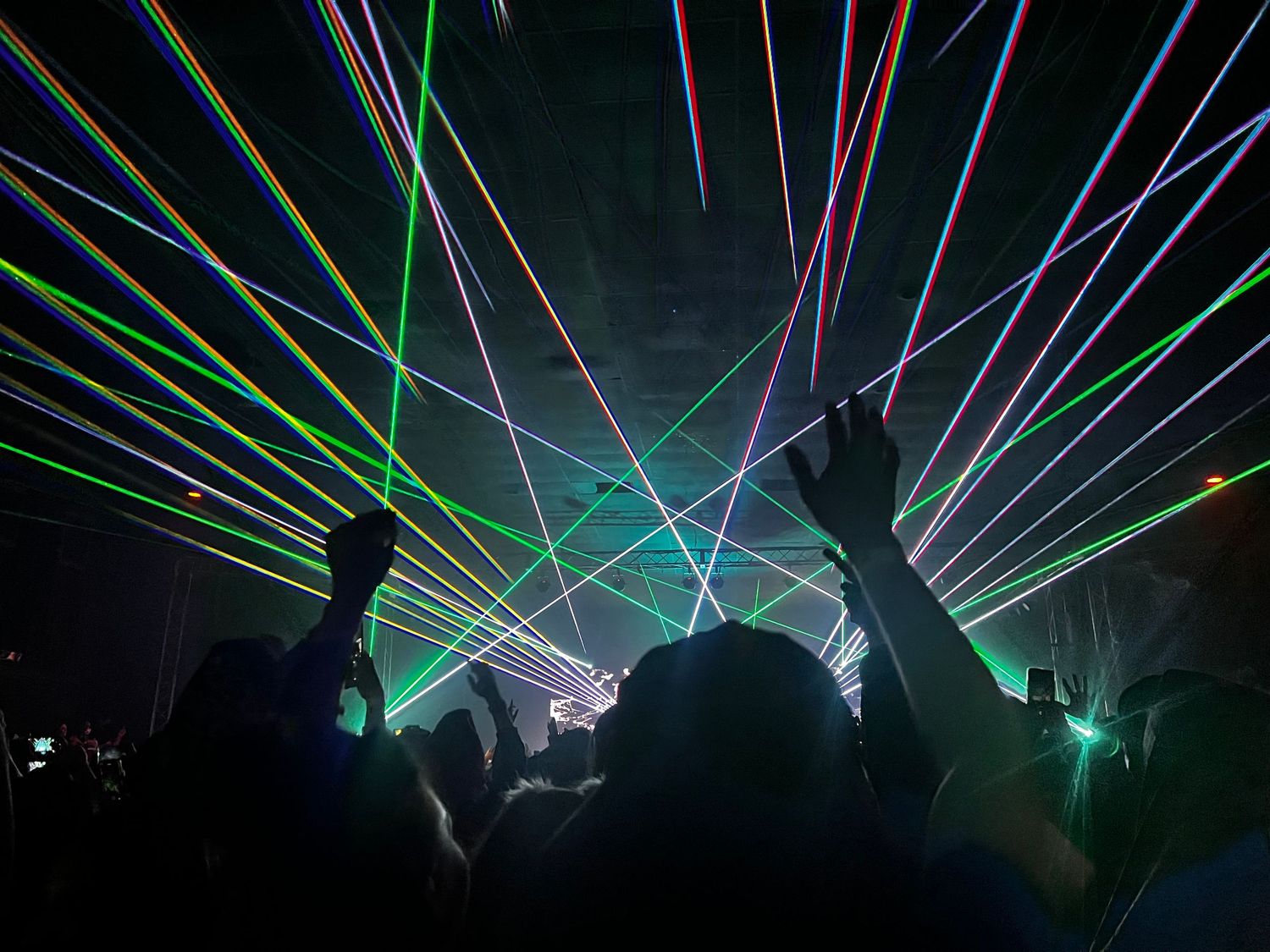 Colorful laser beams cutting through darkness at an electronic music event.