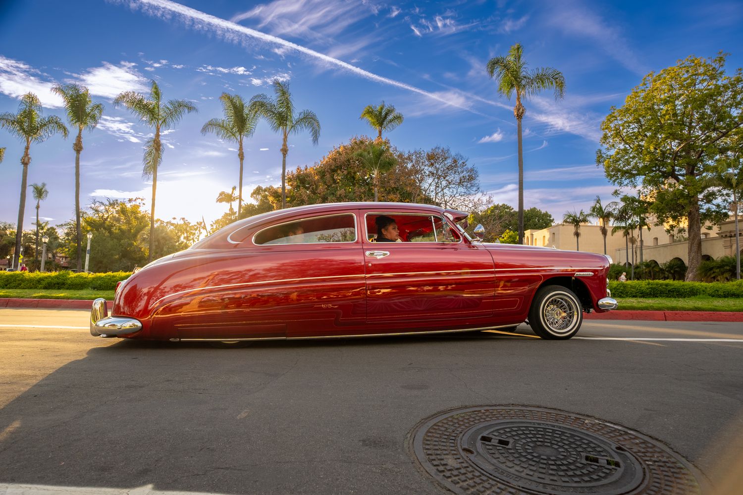 Custom red vintage car with streamlined aerodynamic design parked under palm trees.