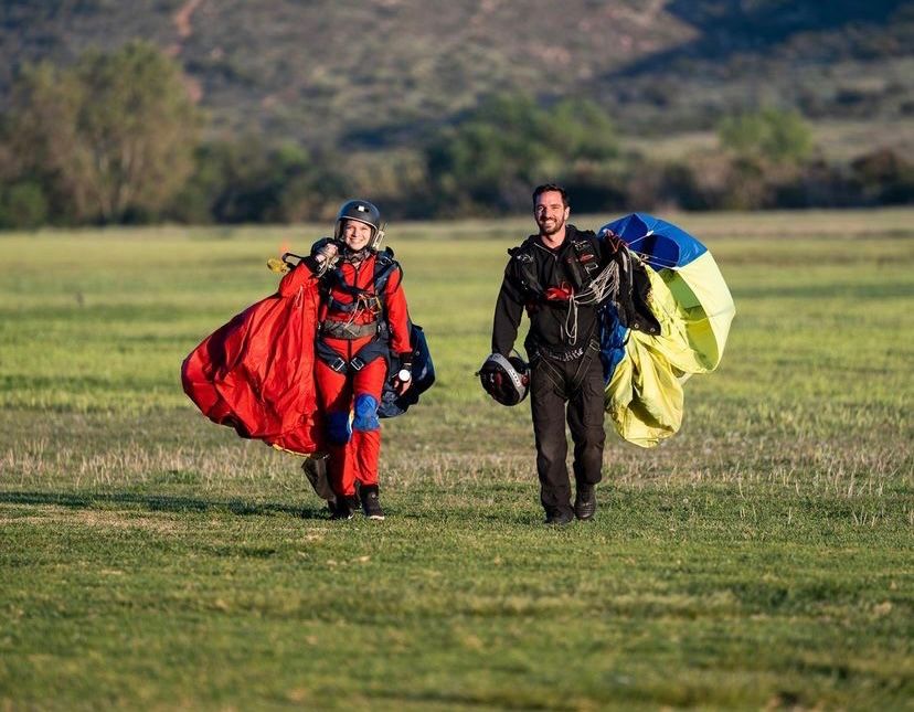 Skydivers with colorful parachutes landing on a grassy field during sunset.