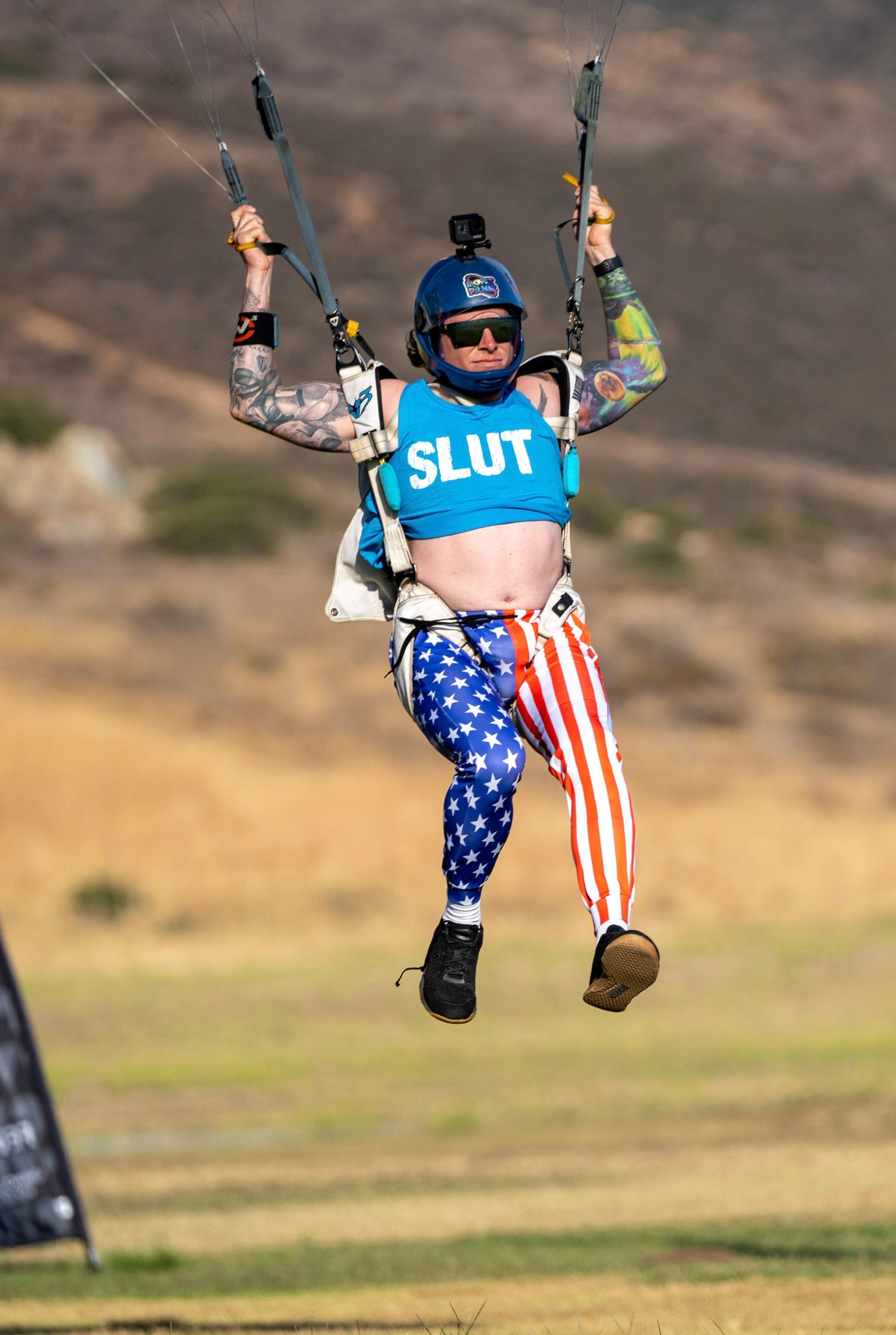 Skydiver in American flag pants and blue top performs a stunt while descending.