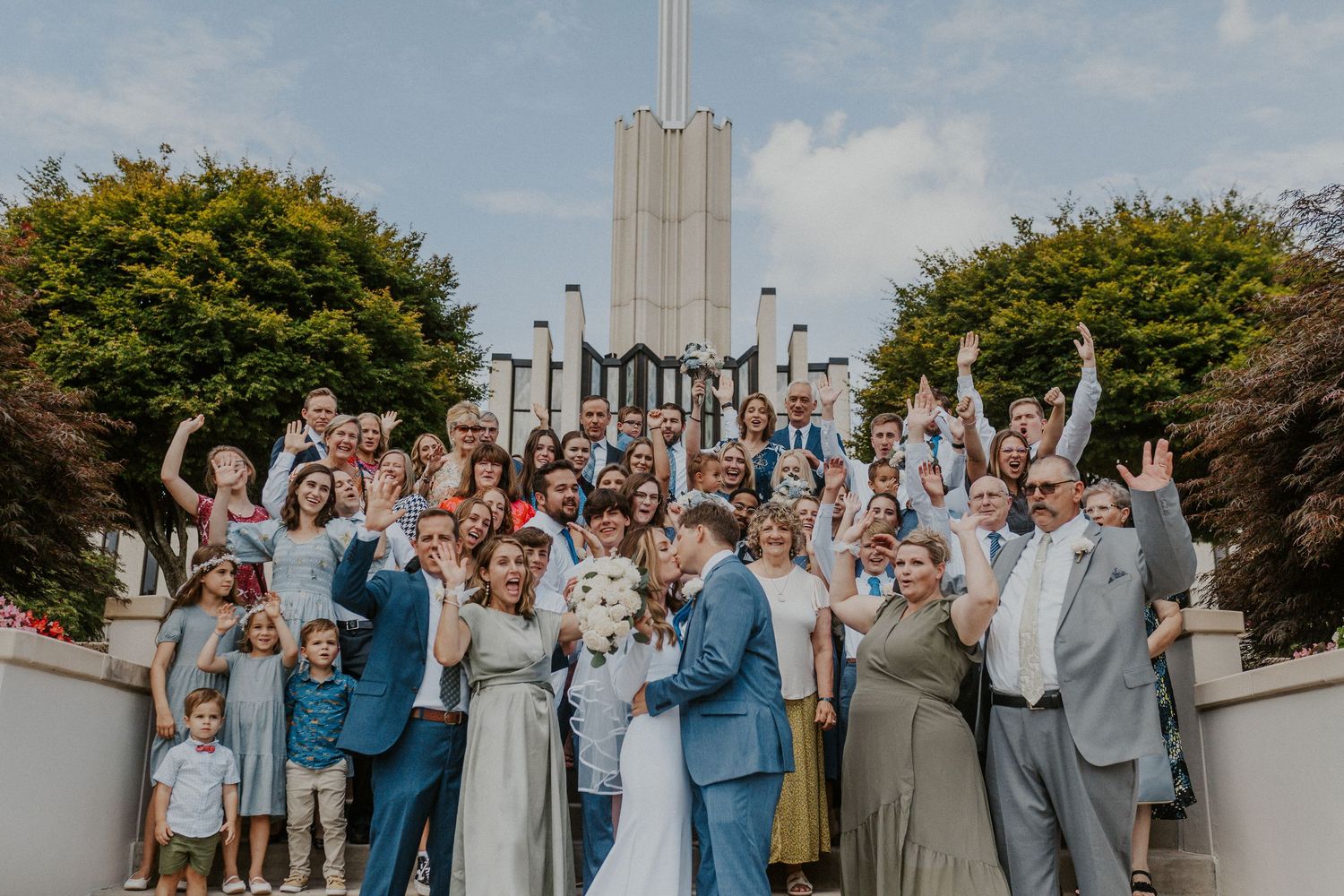 Large group family photo on the steps of a classic wedding venue, capturing the full party with a documentary style.