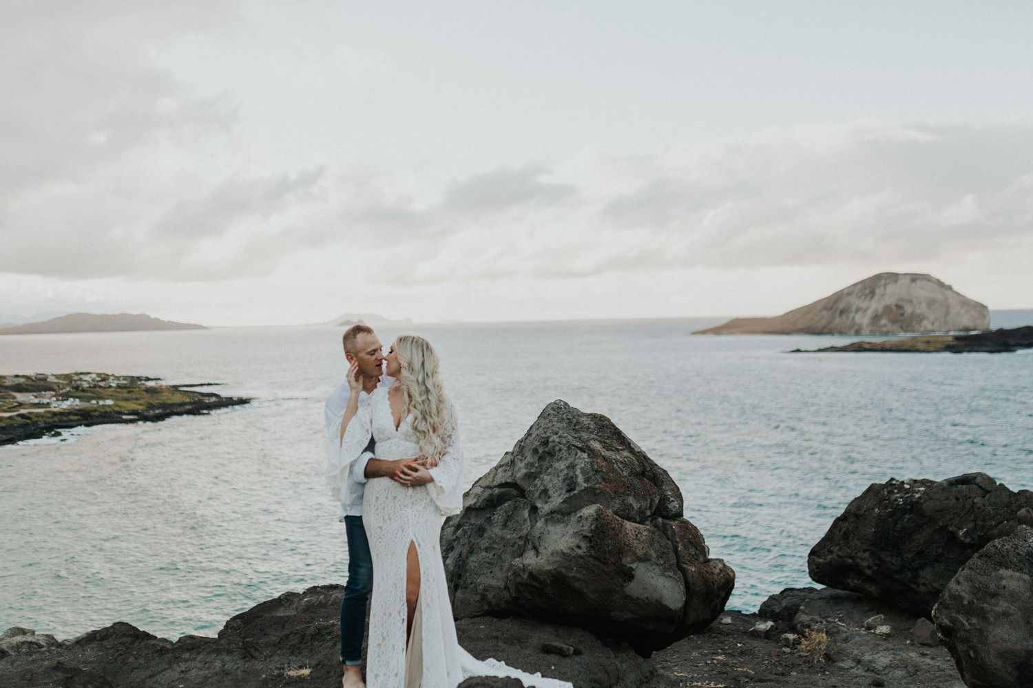 High-End Destination Wedding Photographer capturing couple portrait on dramatic coastal rocks overlooking the turquoise ocean.