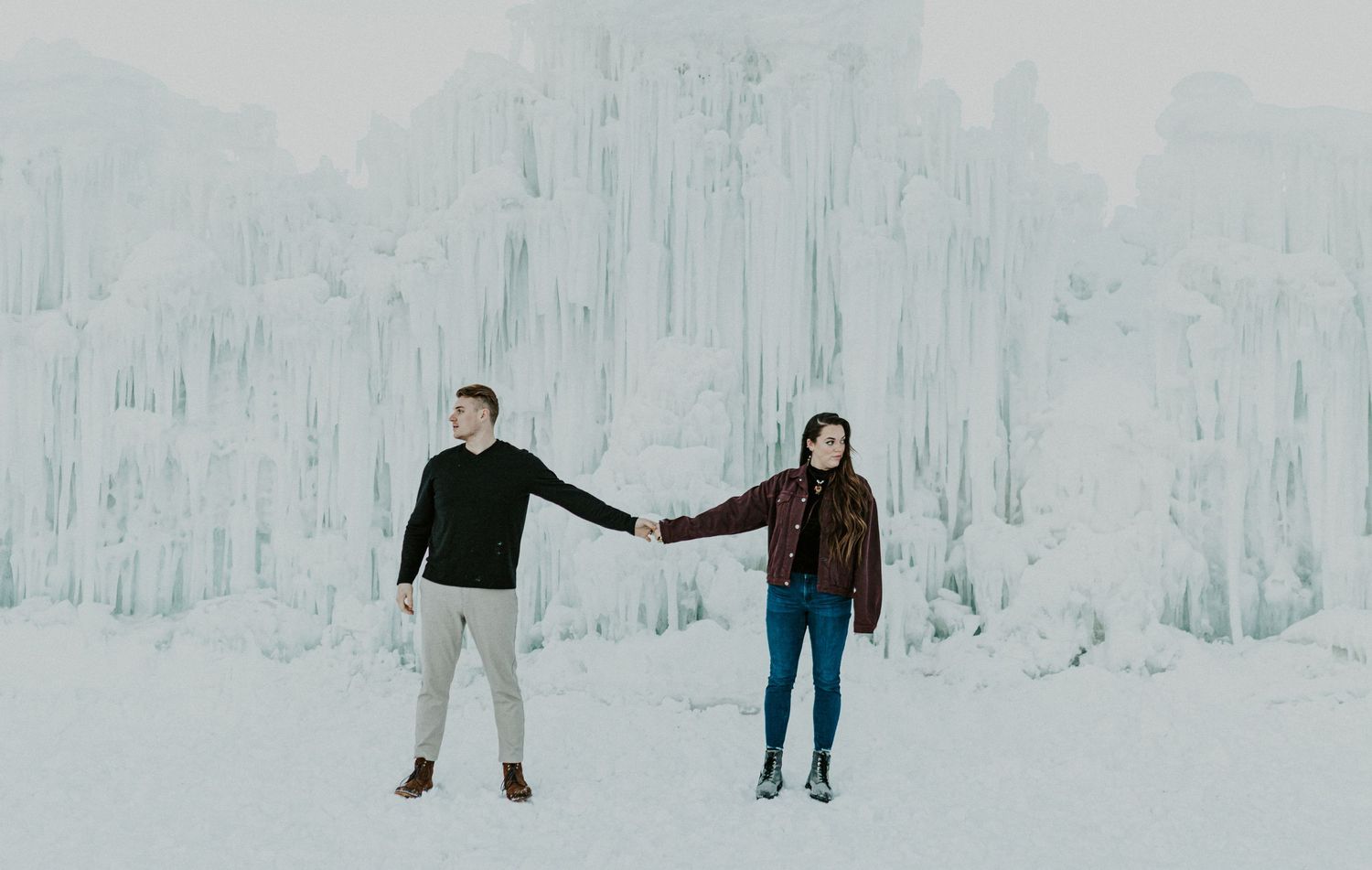 Unique Adventure Elopement photography of a couple standing hand-in-hand in front of a dramatic frozen ice structure. Serving extreme travel