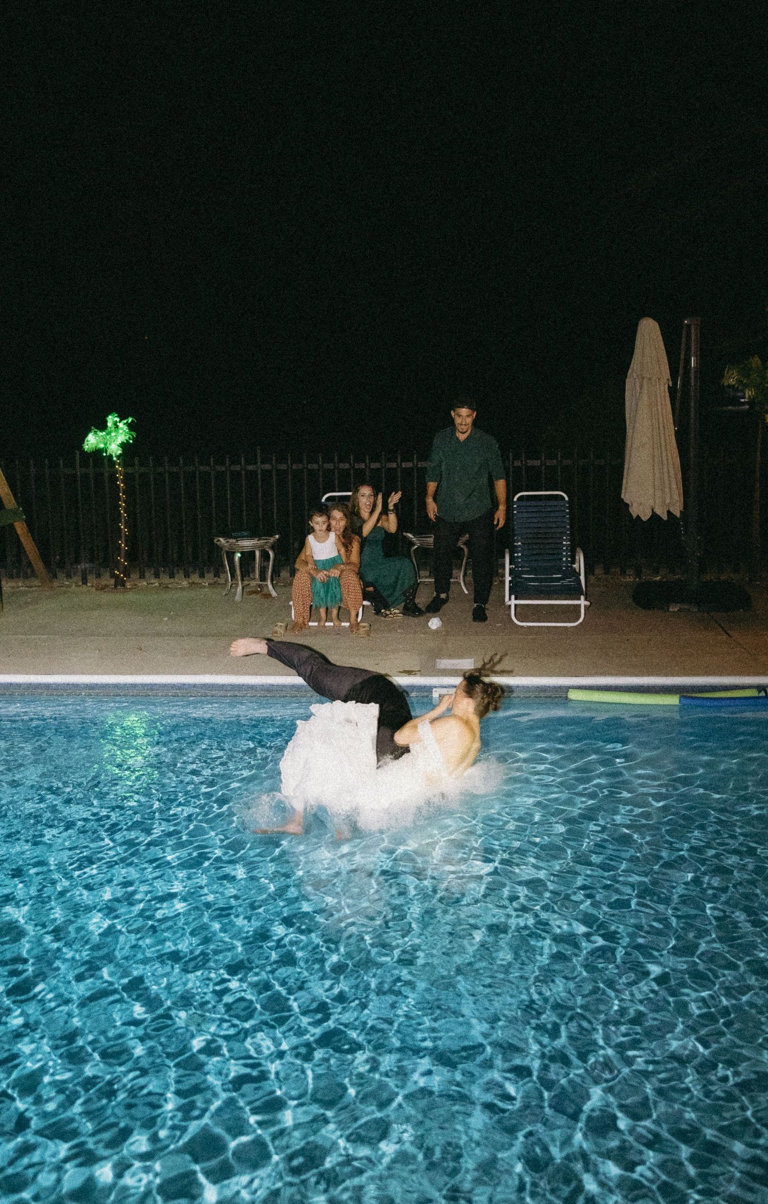 Candid luxury wedding photo of a couple celebrating in a pool at night. Documentary photography for high-end, memorable events.
