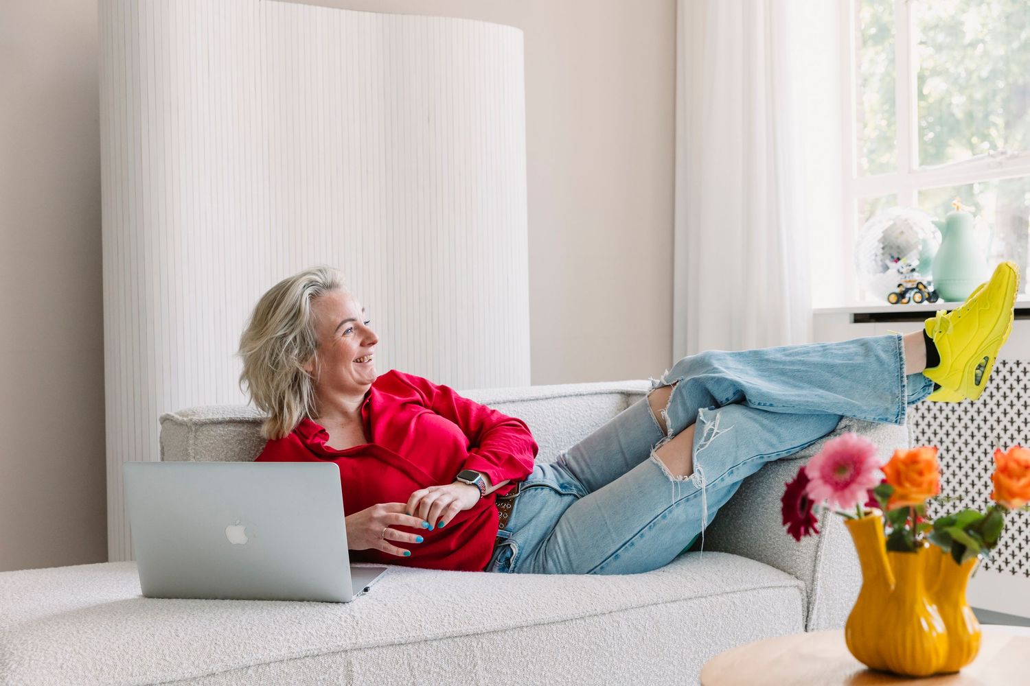 Bright interior room with person resting on couch near colorful throw pillows and yellow kettle.