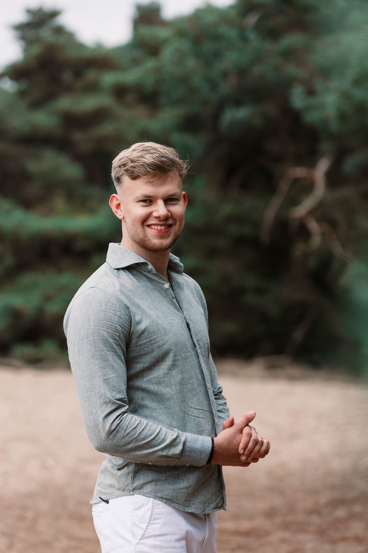 Person wearing grey long sleeve shirt laughing and gesturing outdoors against natural background.