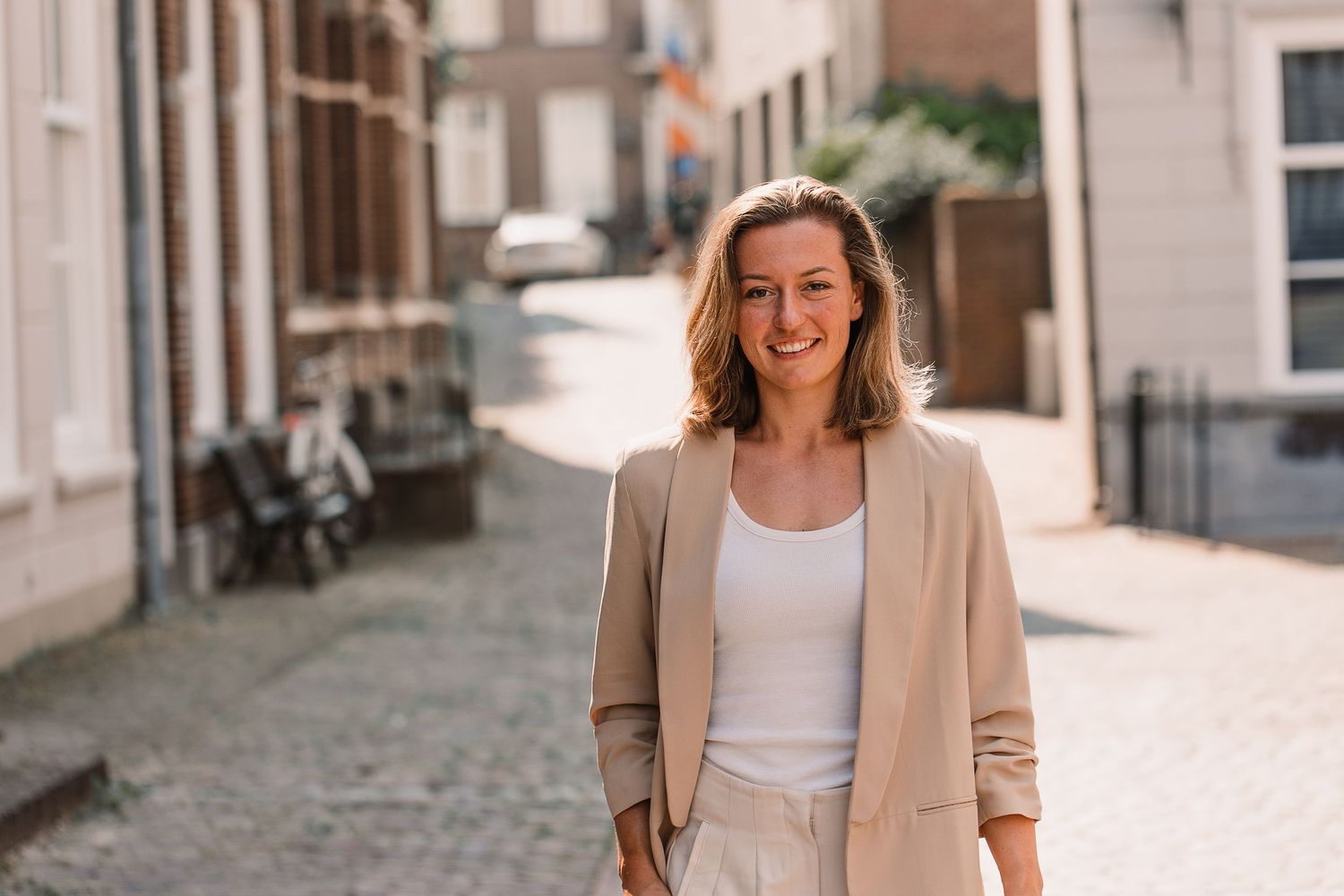 Woman wearing neutral business attire smiles while standing in an urban setting.