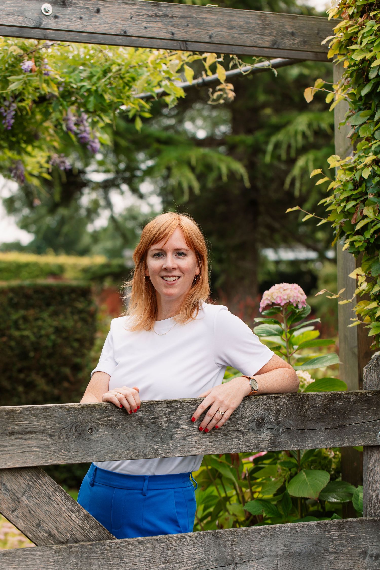 Person leaning on rustic wooden fence in garden setting.