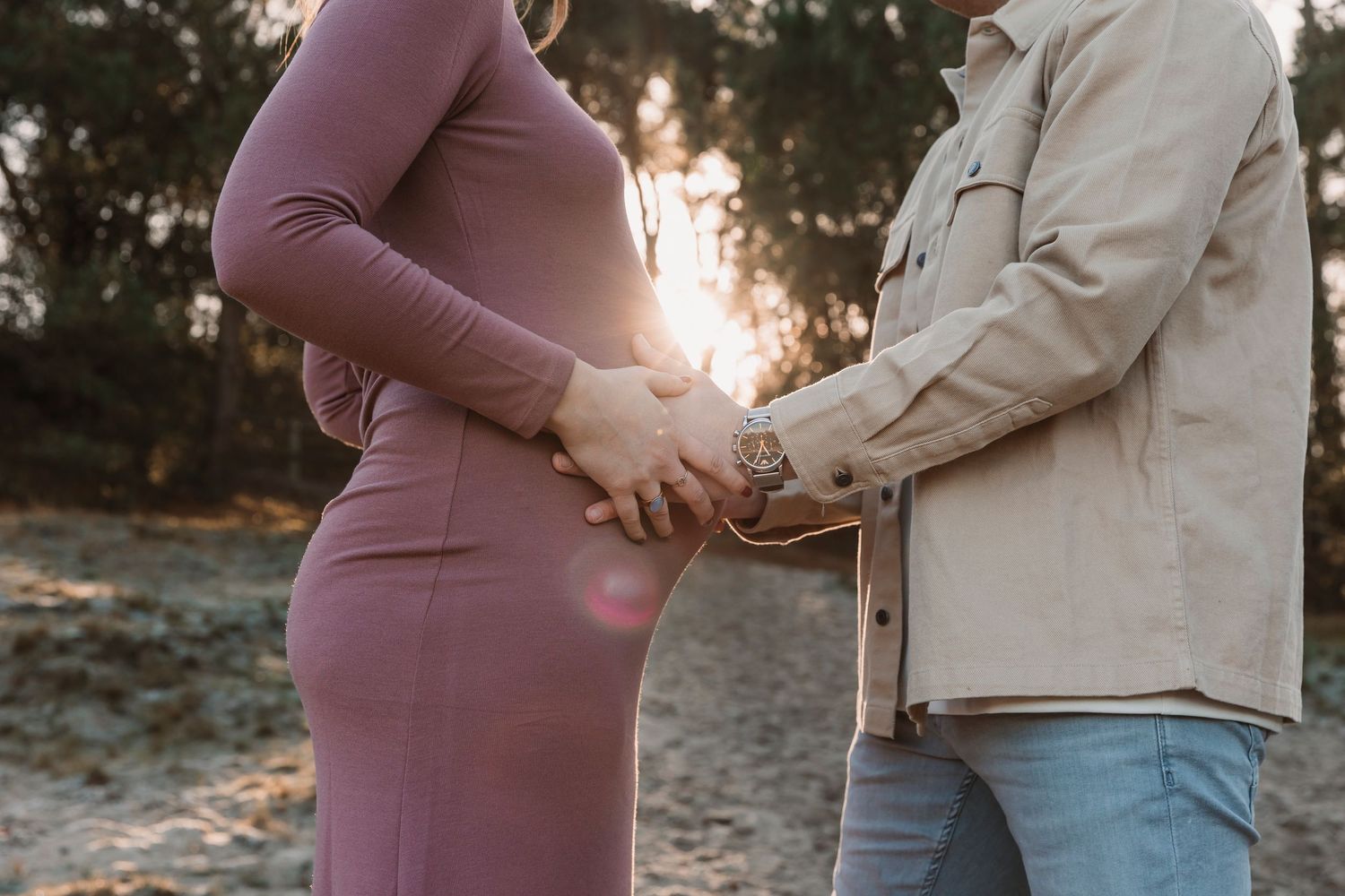 Intimate maternity photo of couple holding hands at sunset.