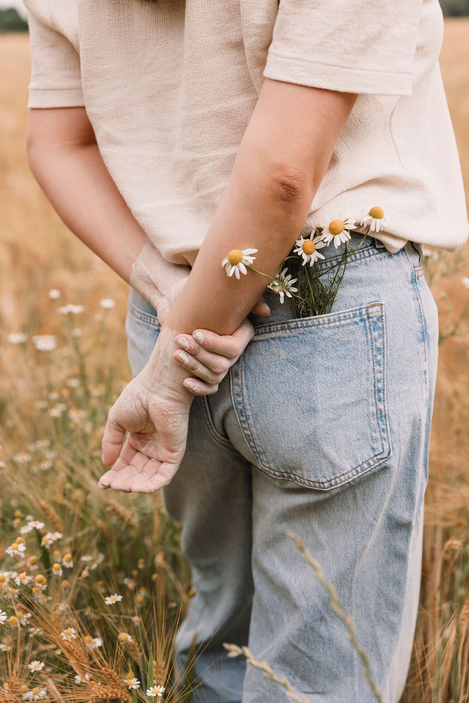 Close-up of hands tucking flowers into back pocket of light wash denim jeans.