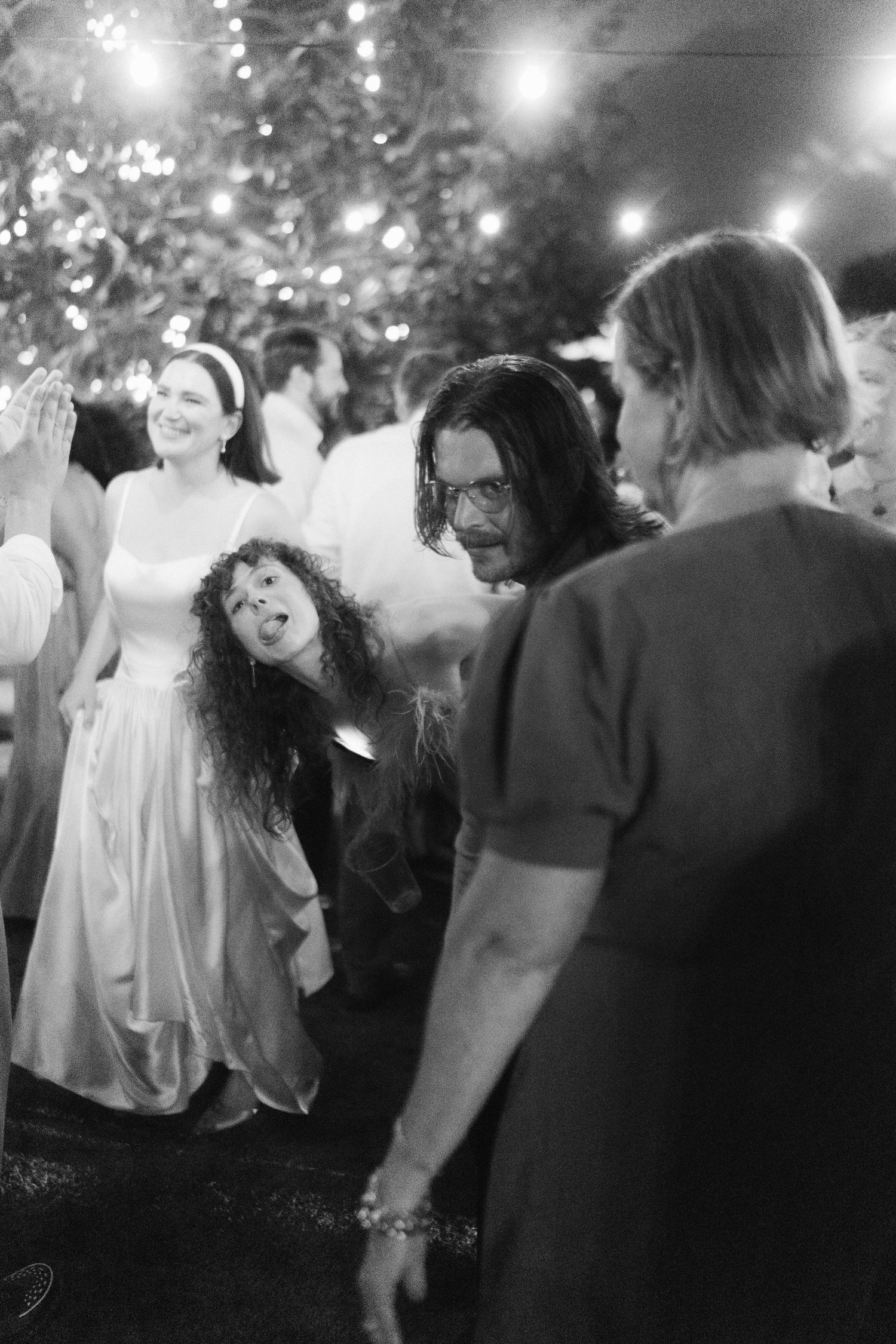 Black and white photo of guests dancing at a wedding reception under twinkling lights.