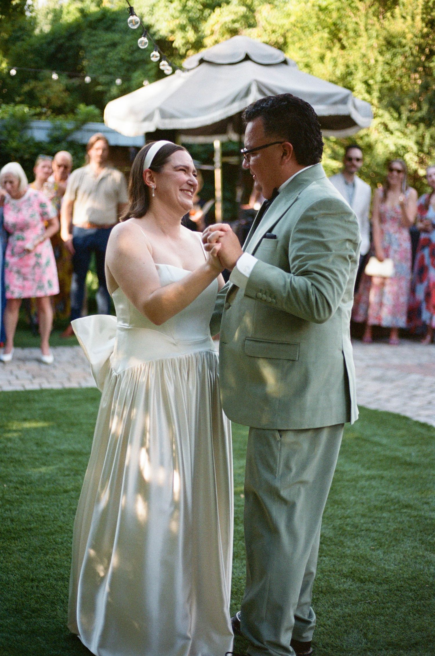A couple shares their first dance at an outdoor wedding reception under a white tent.