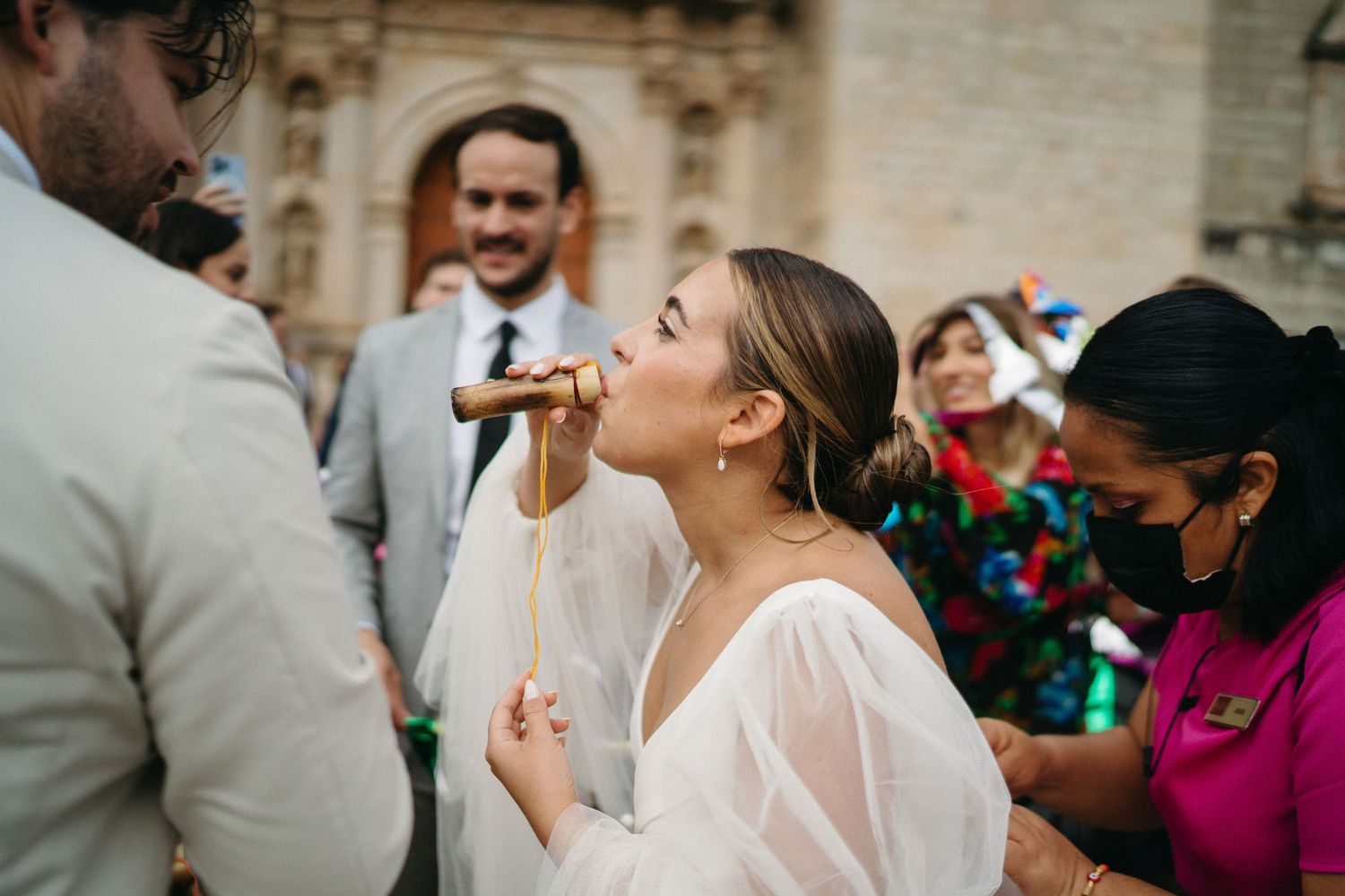 Wedding celebration with guests in colorful attire outside a stone church.