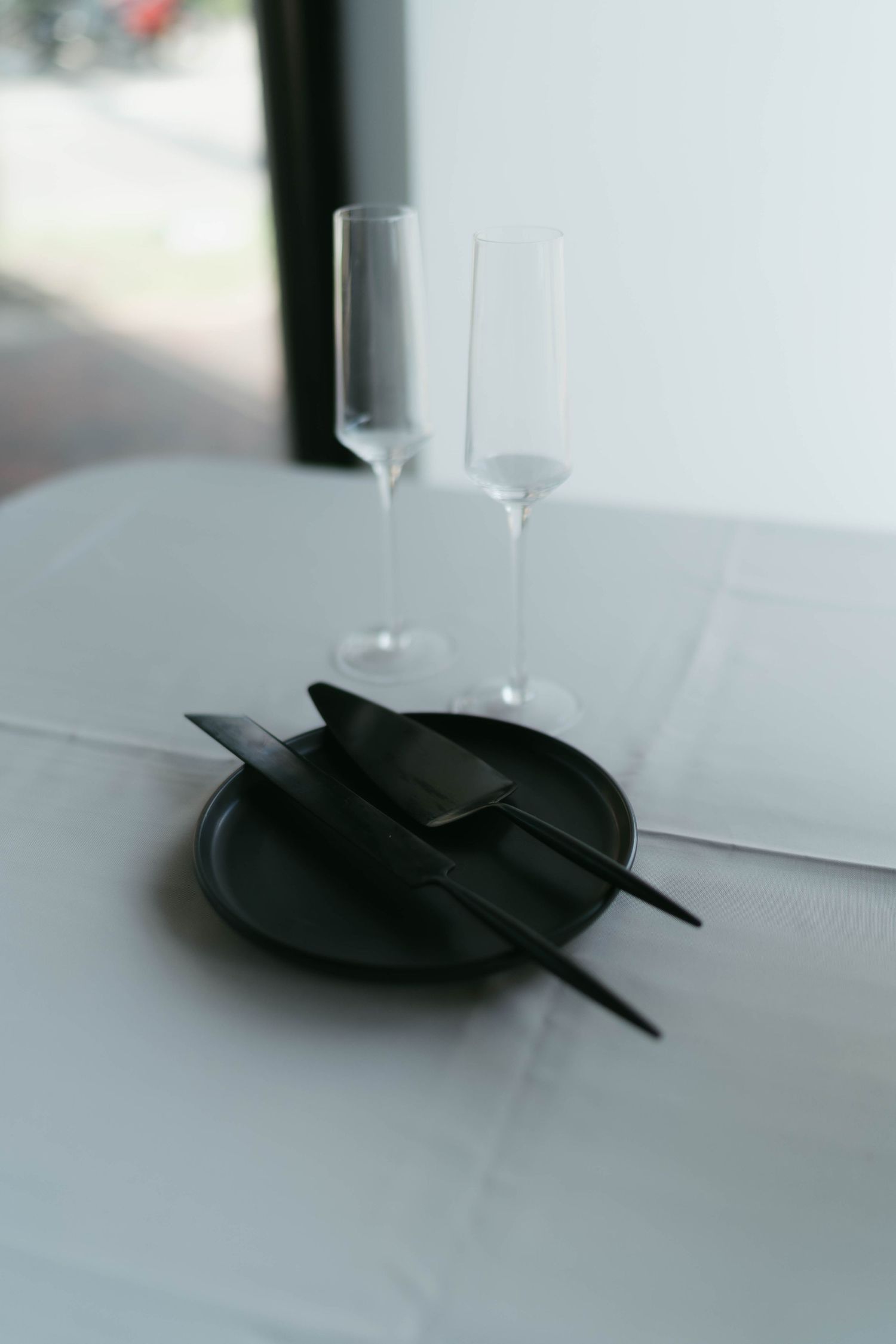 Two empty champagne glasses and black utensils on a white table setting.