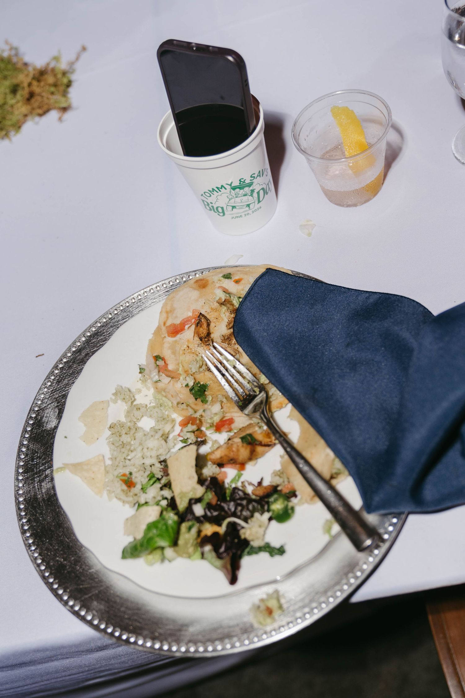 Wedding reception plate with salad, flatbread, and blue napkin beside a phone and drinks.