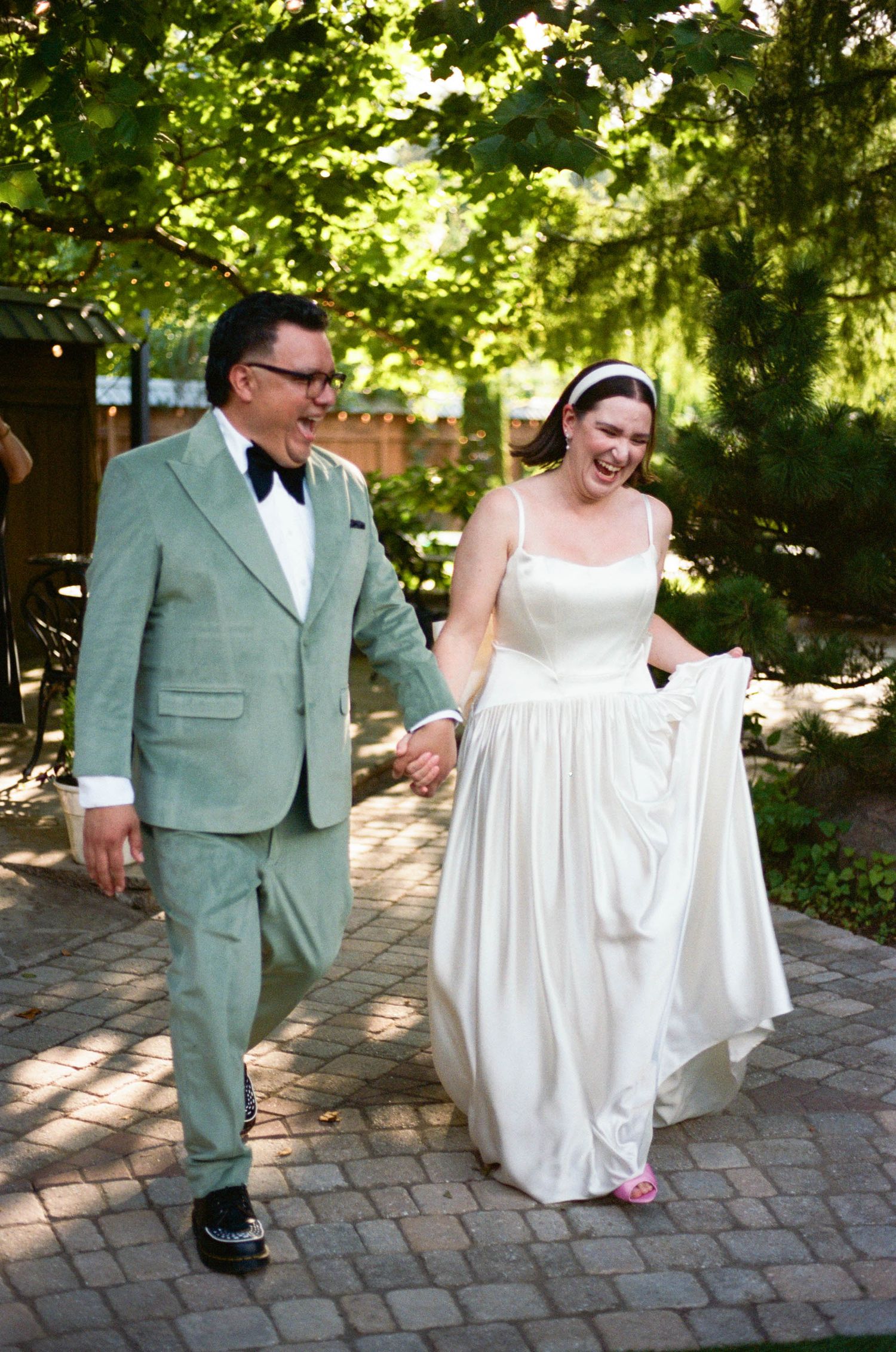 A couple walks together on a brick pathway surrounded by lush greenery.