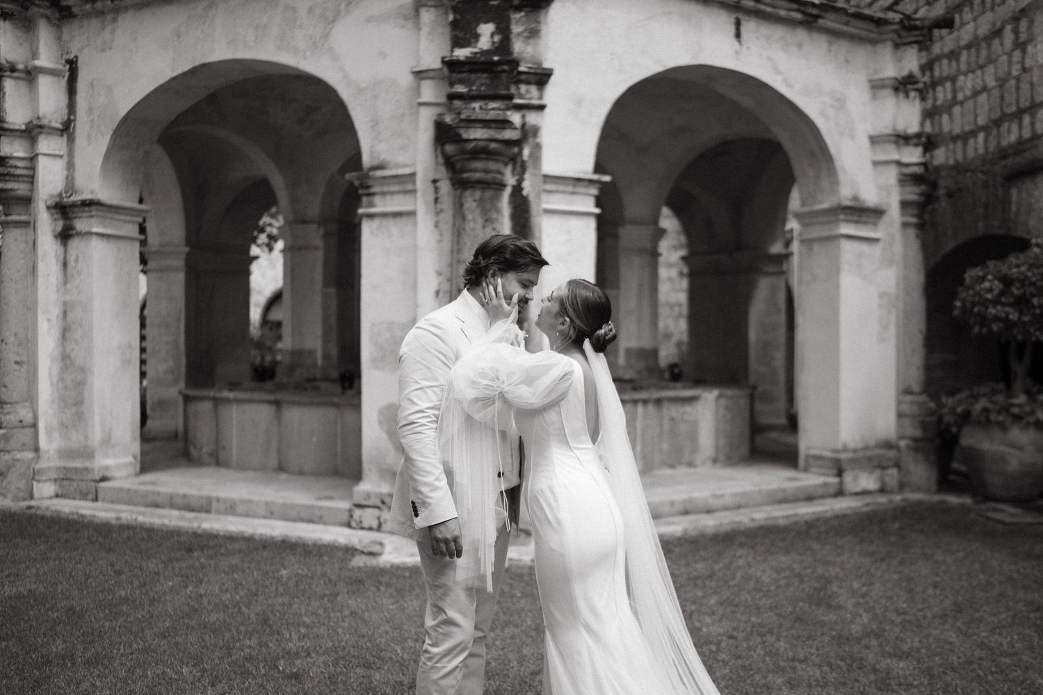 Flowing white wedding dress captured in black and white against architectural backdrop.