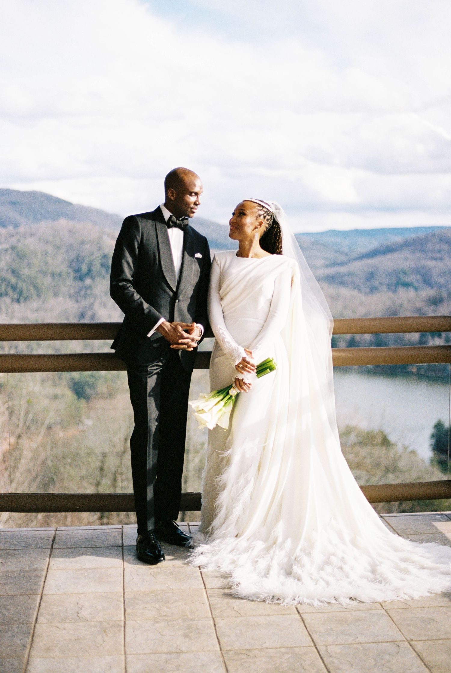 Wedding couple poses on stone terrace overlooking mountain landscape.