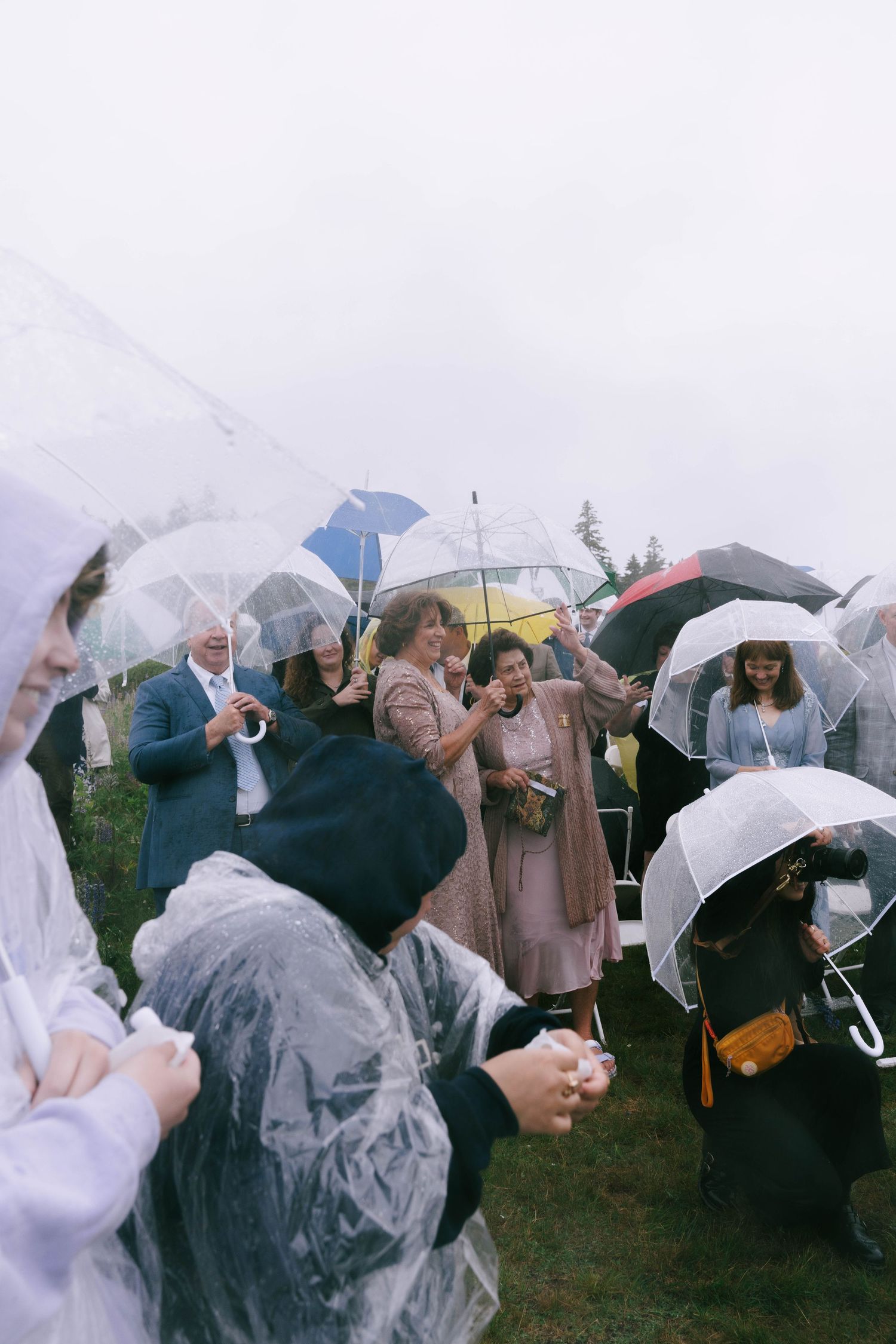 Guests with clear umbrellas gather at a rainy outdoor wedding ceremony.
