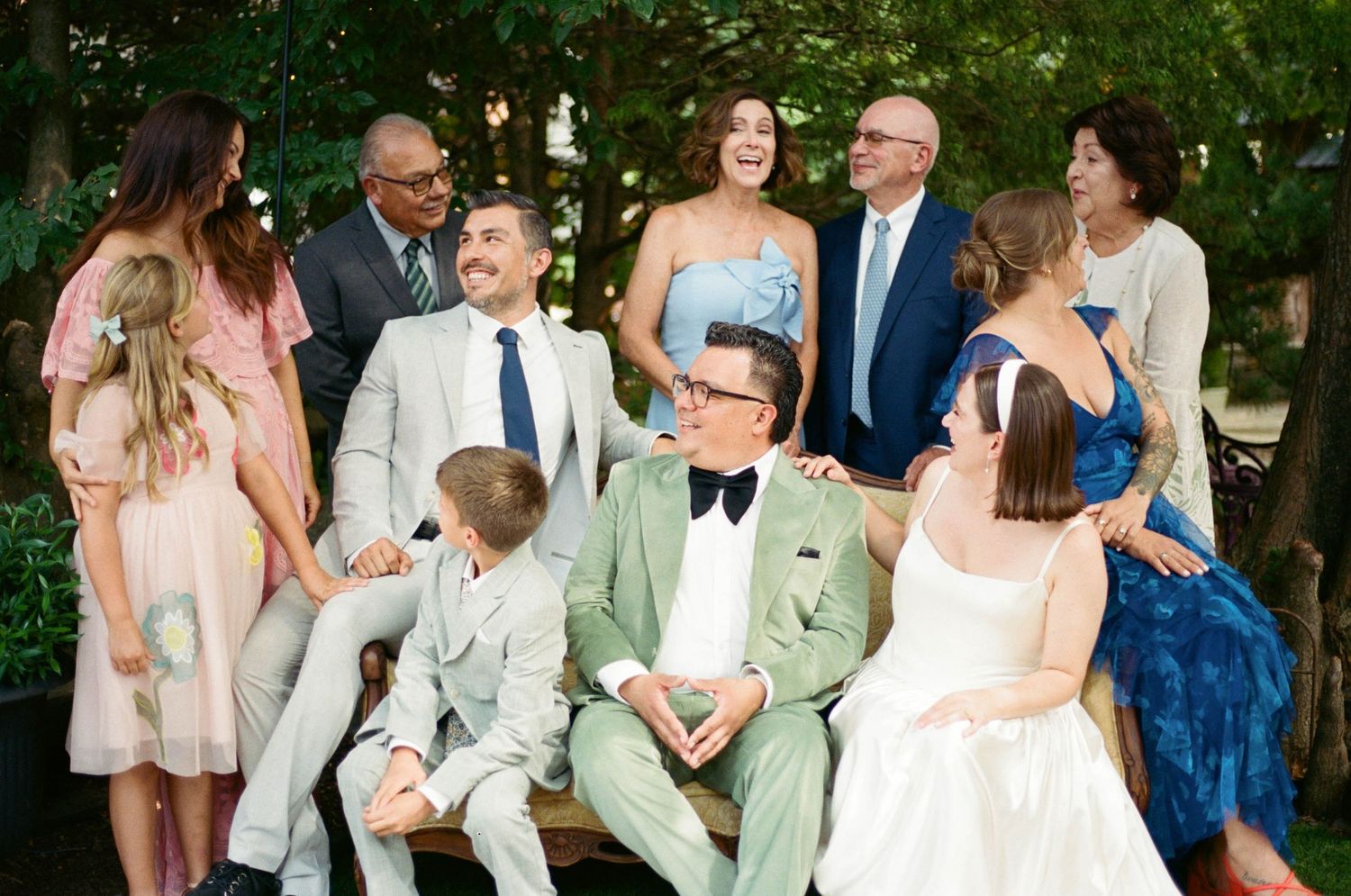 Wedding party gathered outdoors wearing mix of formal attire in mint green and navy blue.