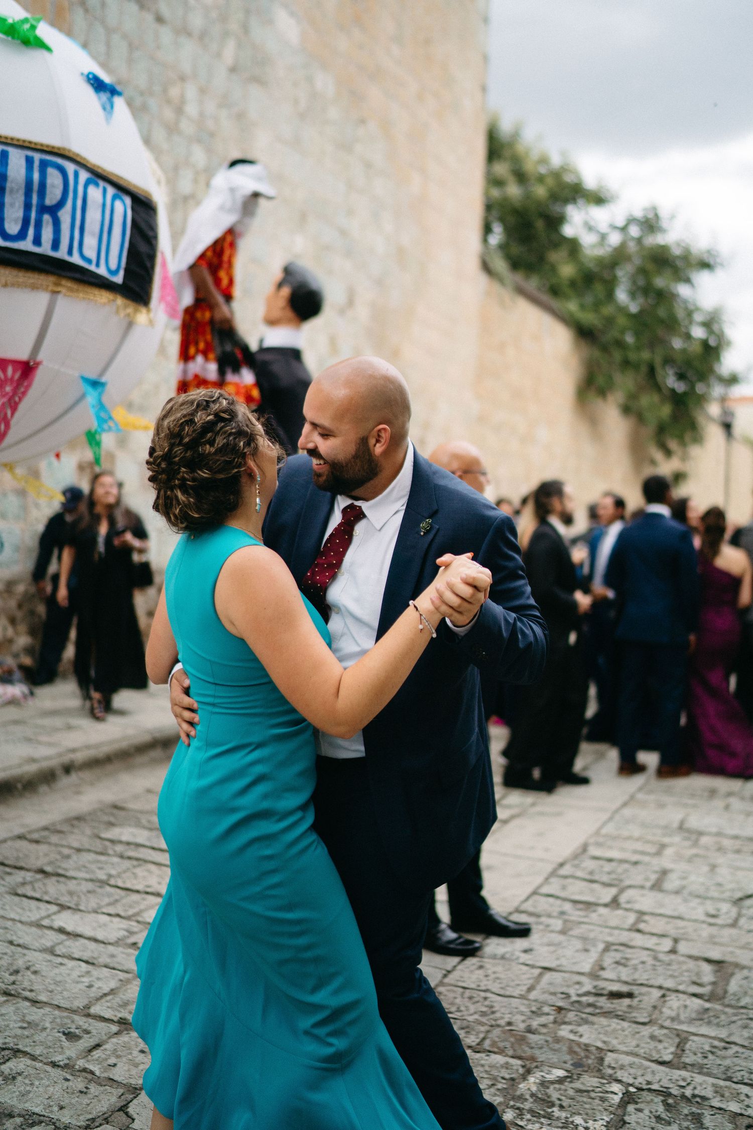Couples dancing together at outdoor wedding celebration with stone wall backdrop.