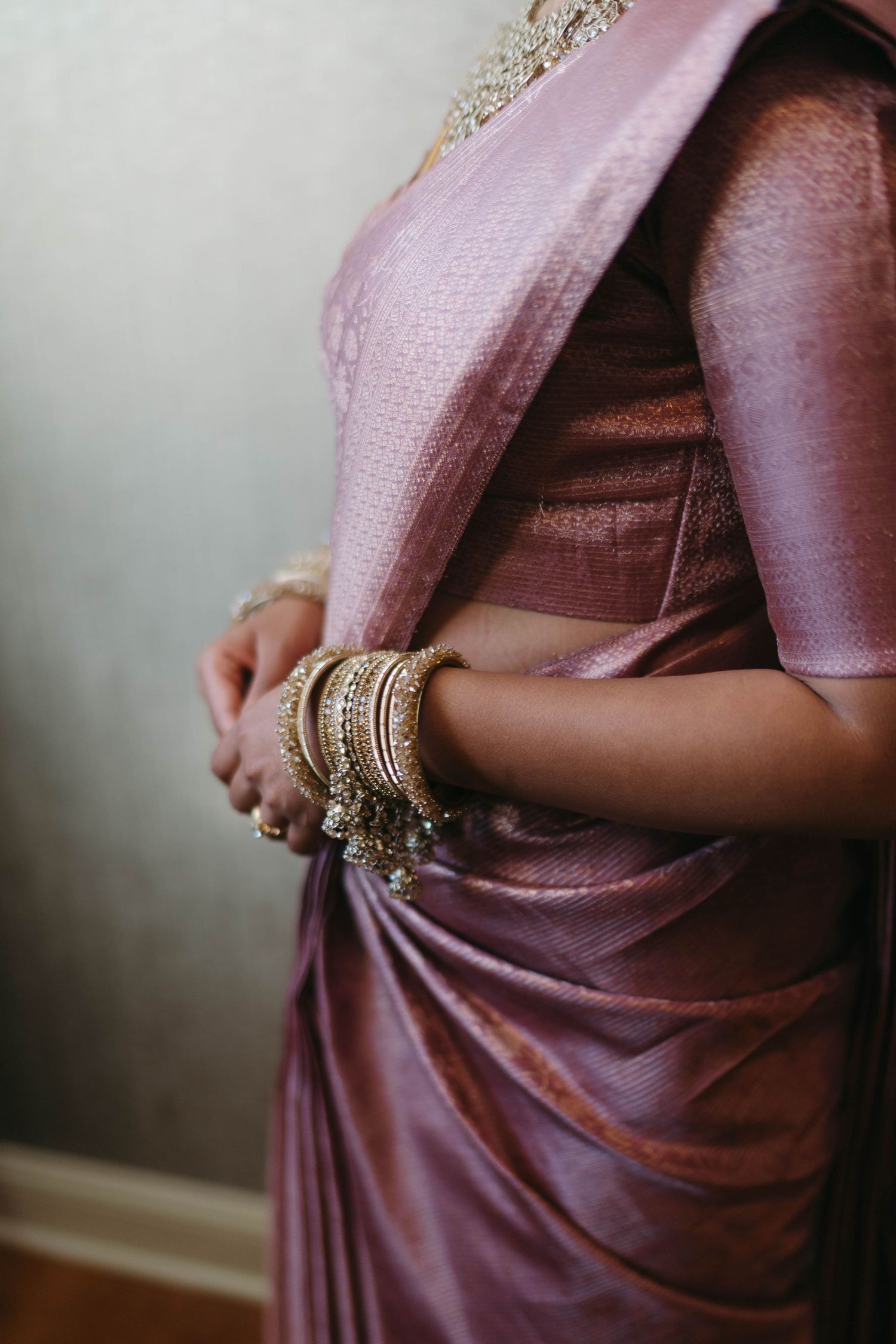 Close-up of bride in pink silk saree adorned with gold bangles and traditional Indian bridal jewelry.