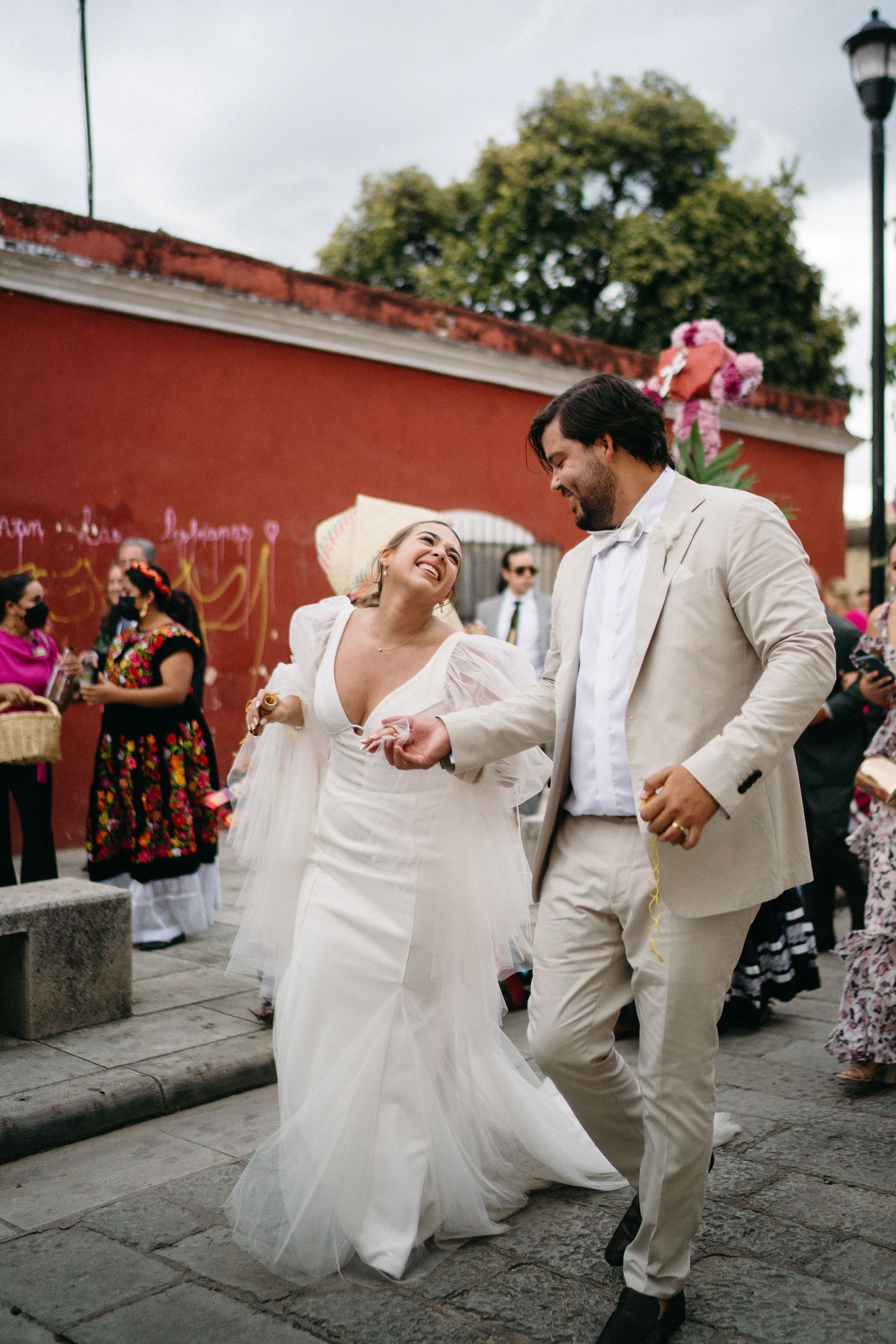 Wedding couple dances playfully on cobblestone street during celebration.