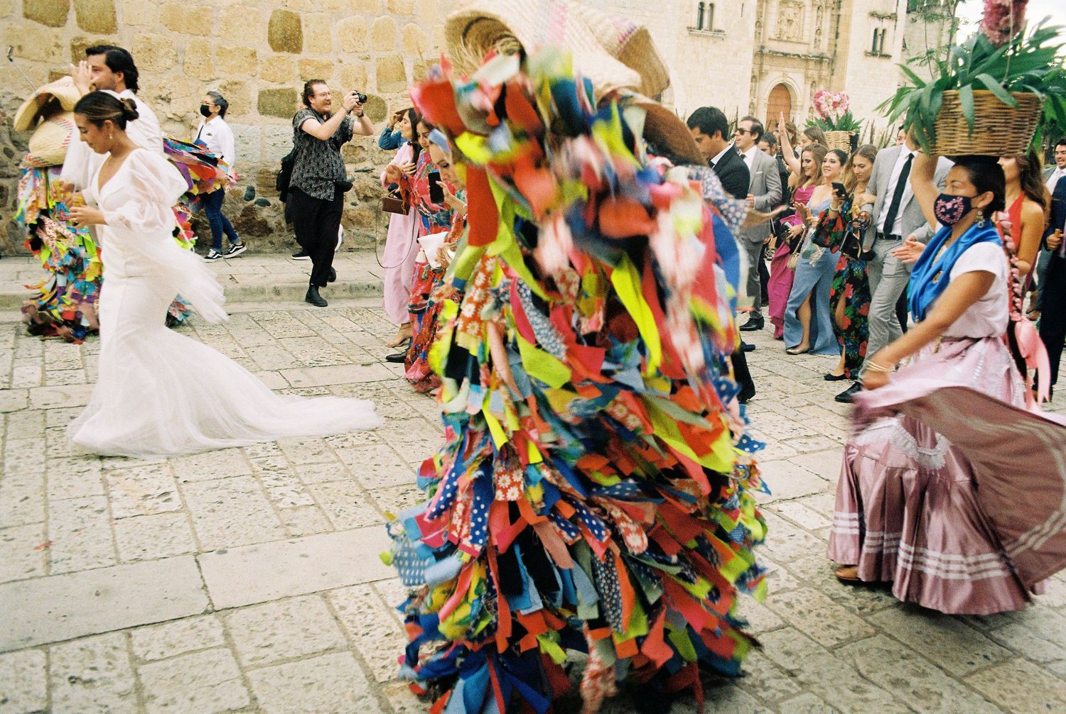 Festival dancers in vibrant traditional costumes perform in a colonial street setting.