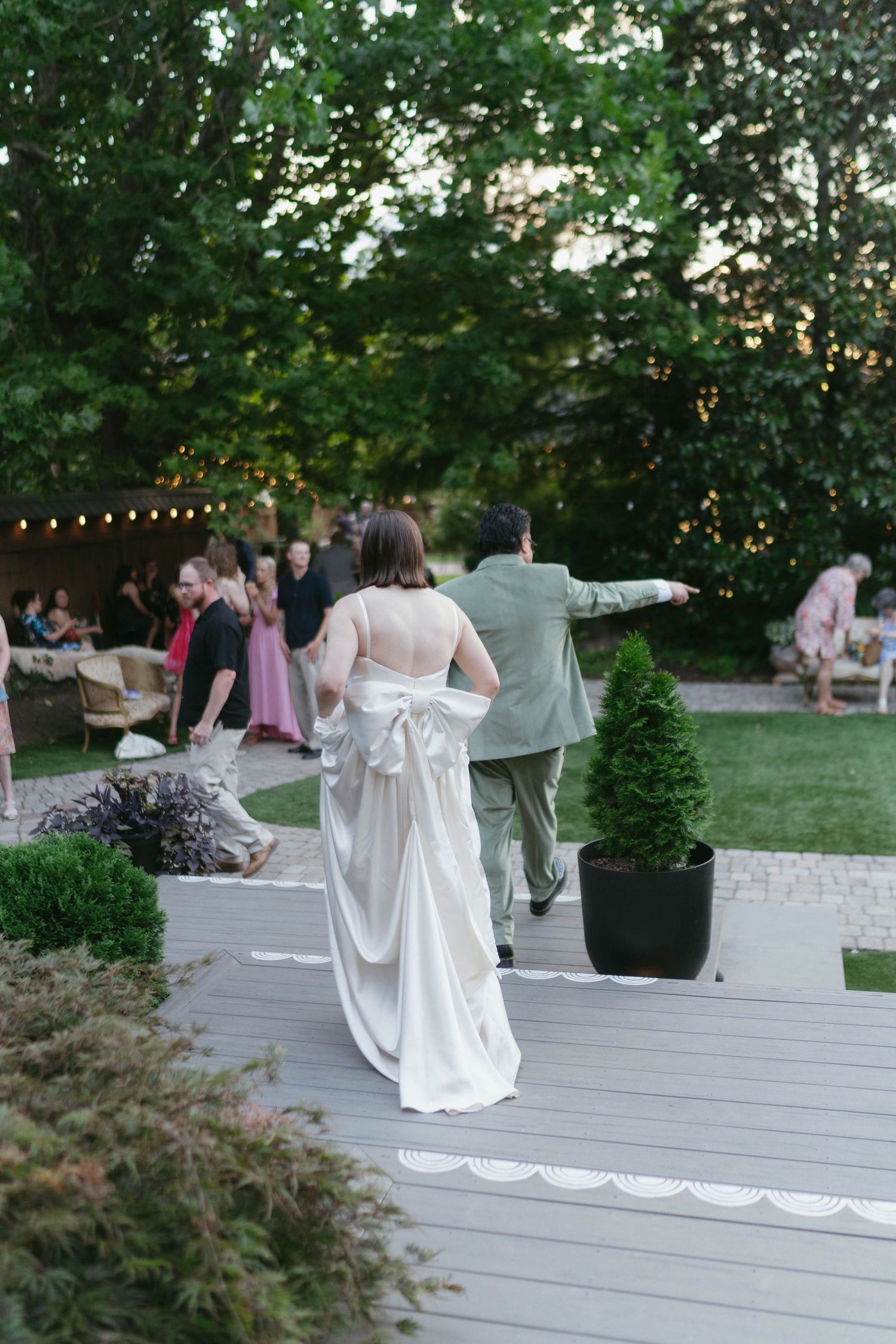 String lights illuminate an outdoor wedding reception deck as guests mingle in the evening.