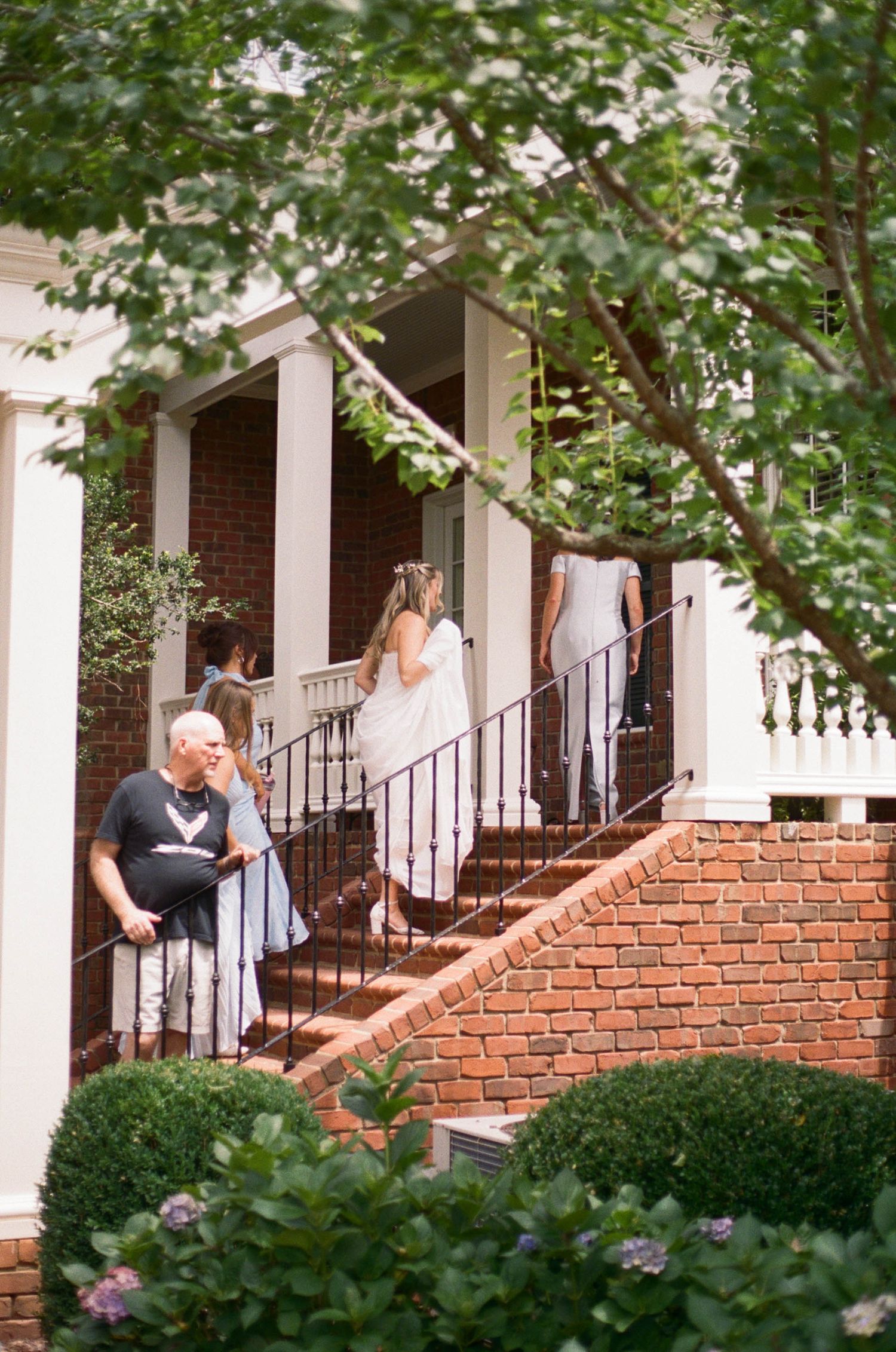 Wedding party descends brick steps of classic white-columned brick manor house.