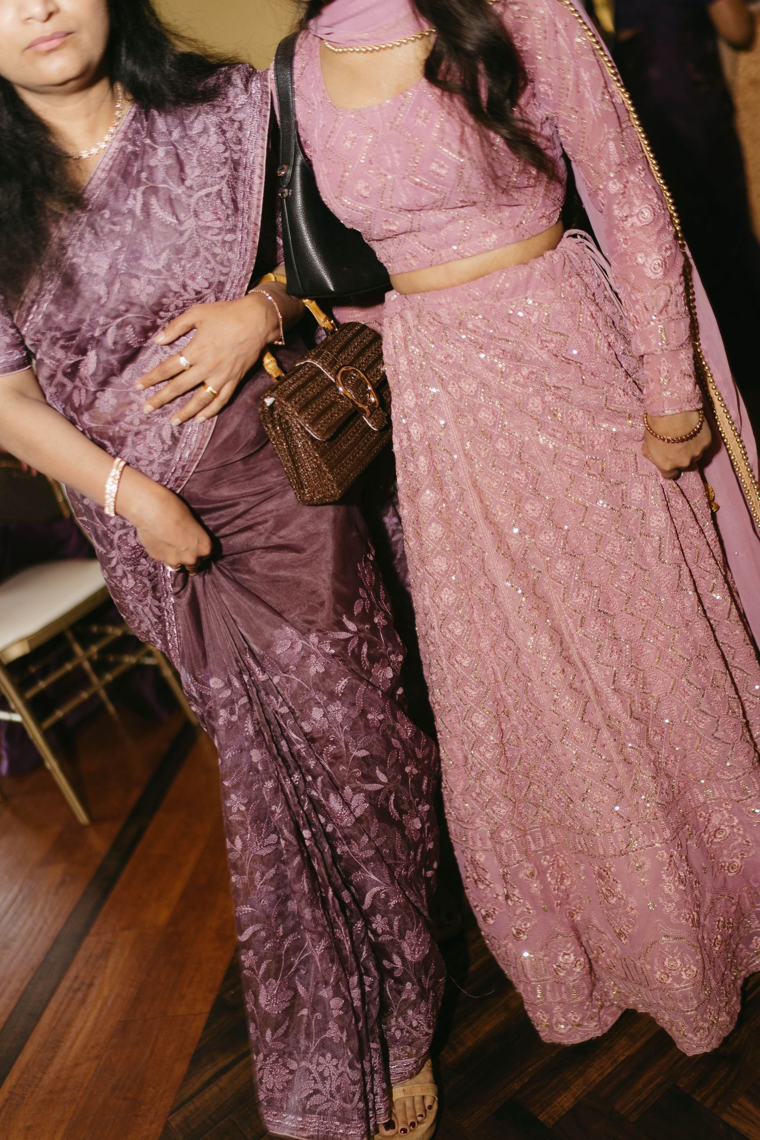 Two women in ornate purple and pink embroidered Indian saree and lehenga at a wedding celebration.