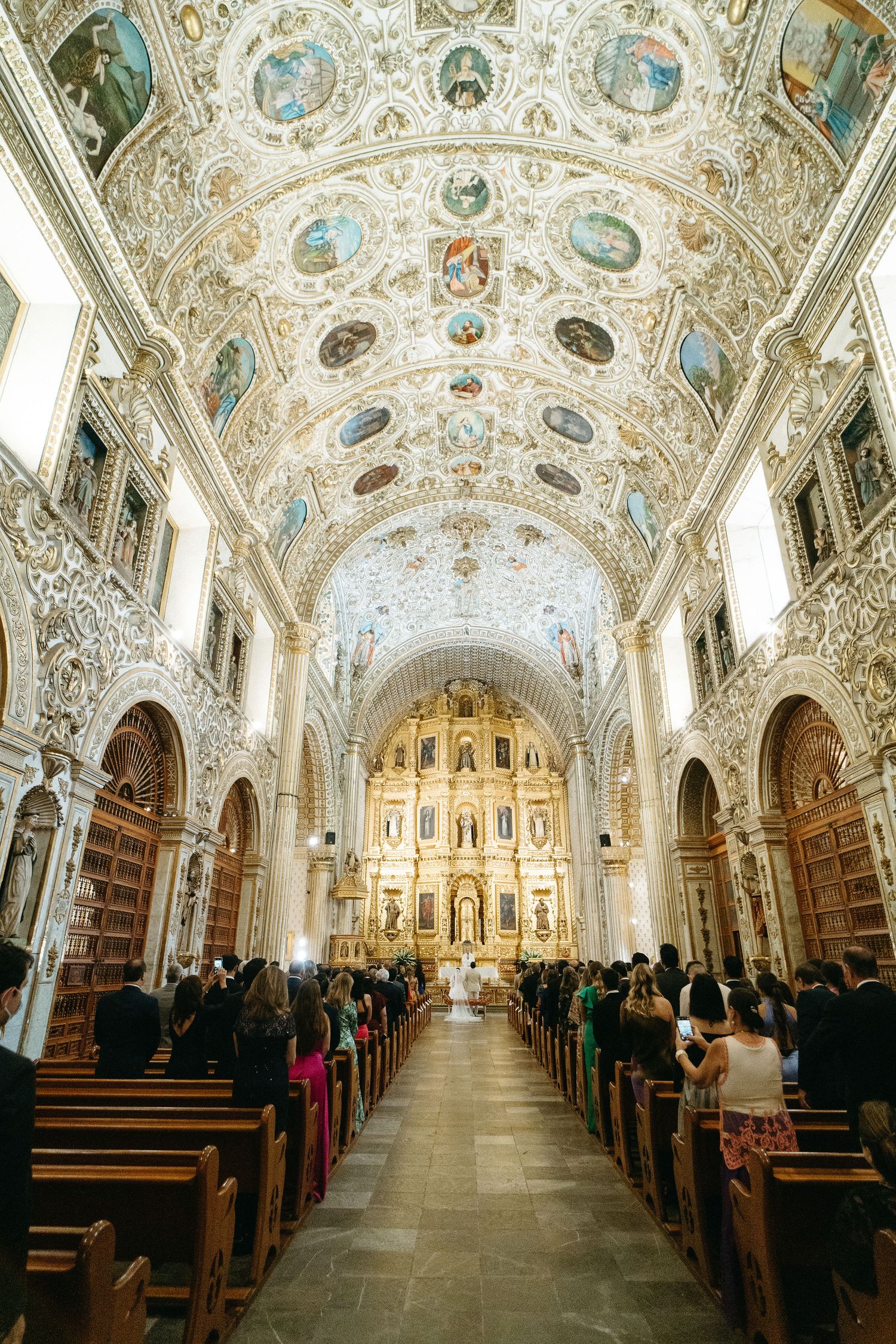 Ornate baroque church interior with decorated ceiling and long aisle lined with wooden pews.