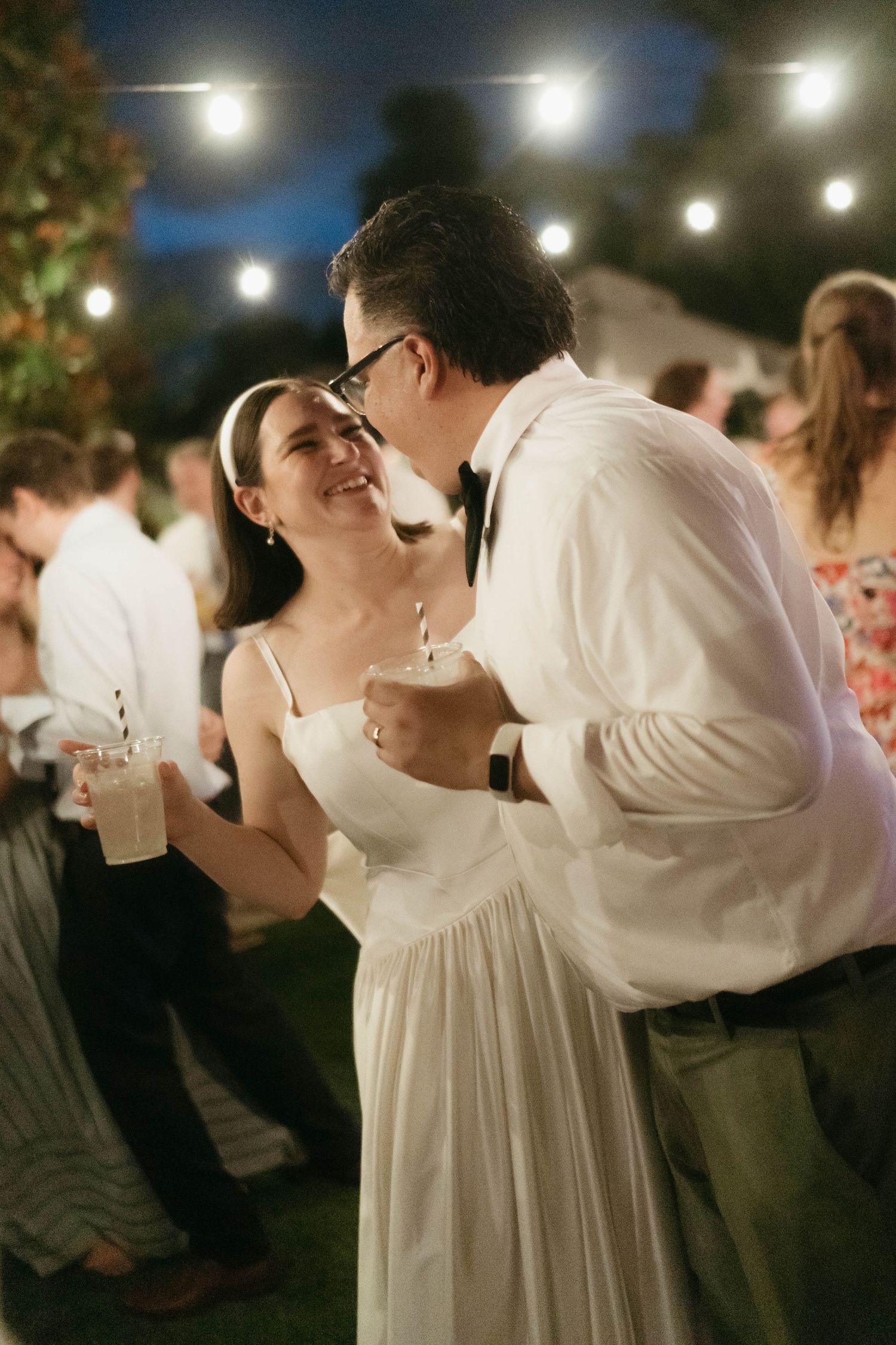 Couple sharing a romantic dance moment under twinkling lights at an outdoor wedding reception.