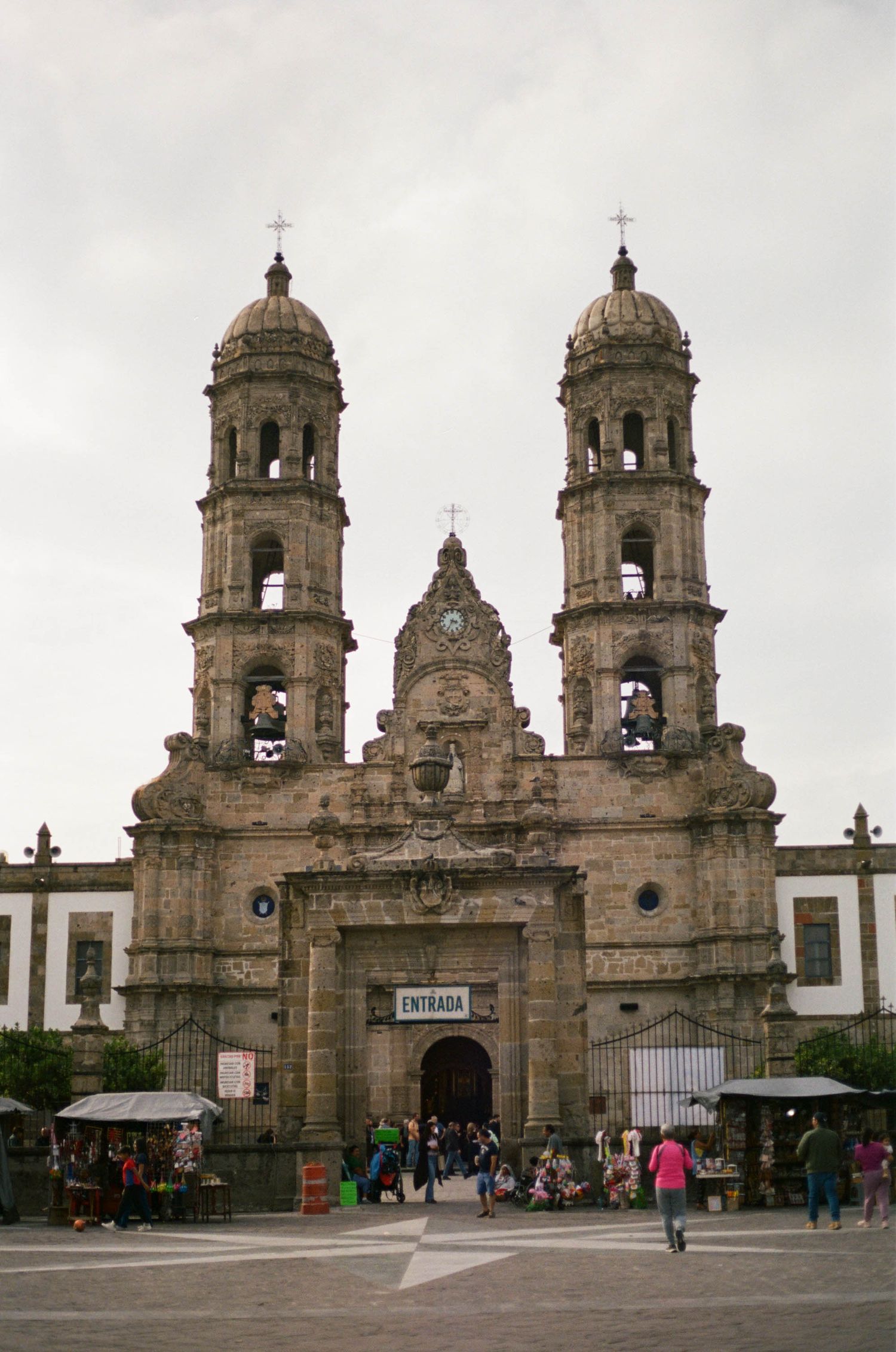 Historic stone church with twin bell towers and ornate baroque architecture in a Mexican town square.
